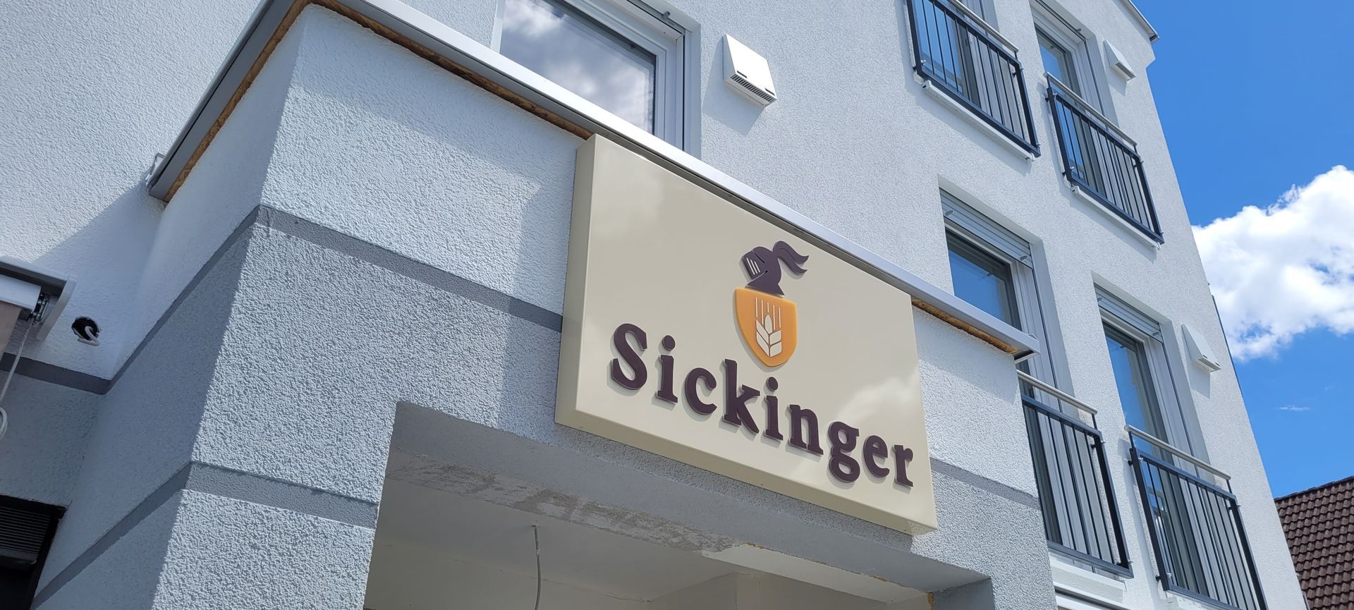 Leuchtkasten für das Restaurant „Sickinger“ an einem weißen Gebäude.