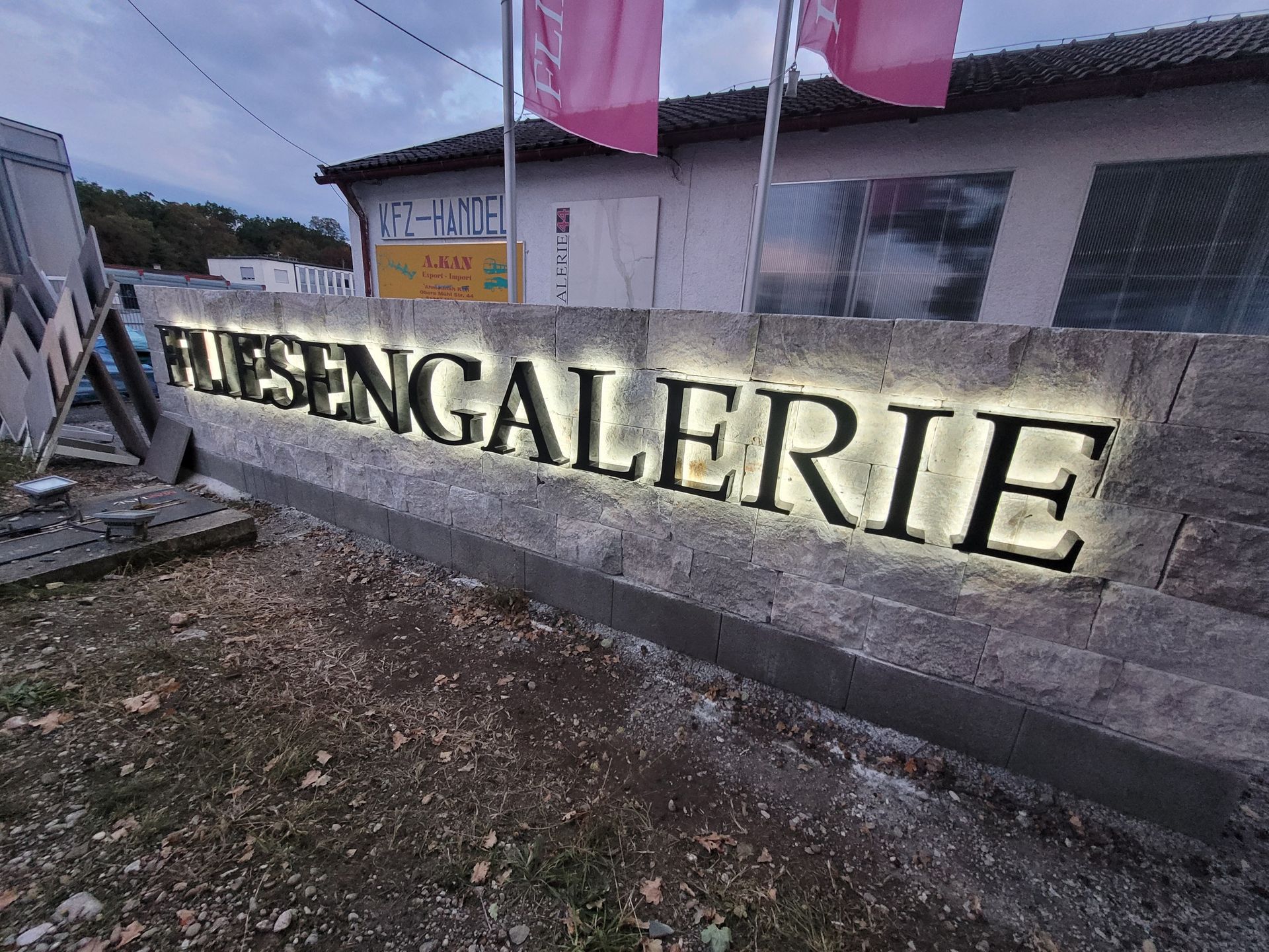 Beleuchtetes „FLIESEN GALERIE“-Schild an einer Backsteinmauer.