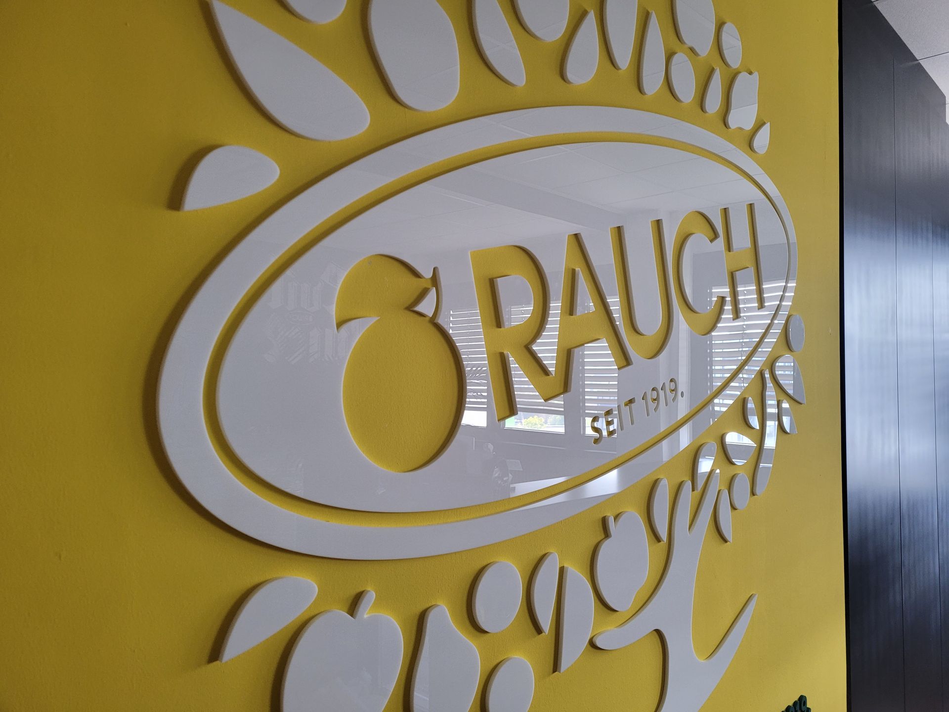 RAUCH-Logo in Weiß auf gelber Wand mit Blatt- und Fruchtakzenten.