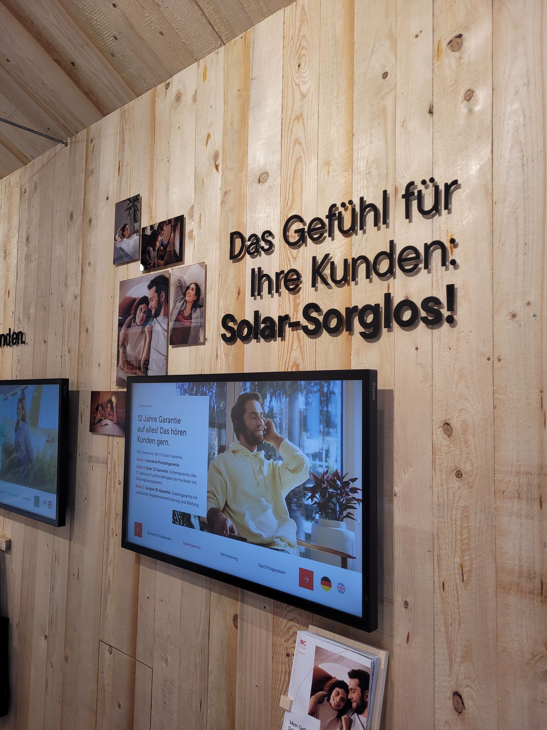 Holzwand mit Fernsehbildschirmen, Fotos und deutschem Text „Solar-Sorglos“.