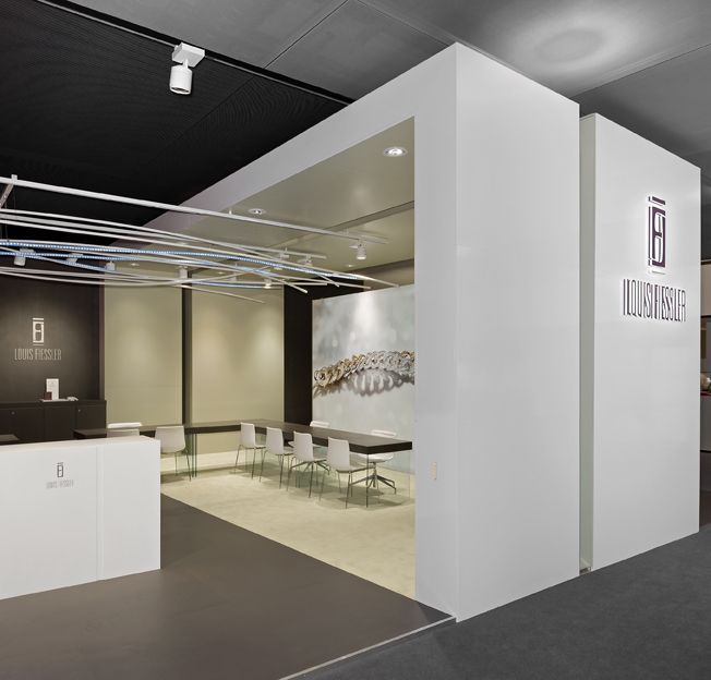 Moderner Messestand mit weißen Wänden, Konferenzbereich und Logo für „ILLUMINABLE“.
