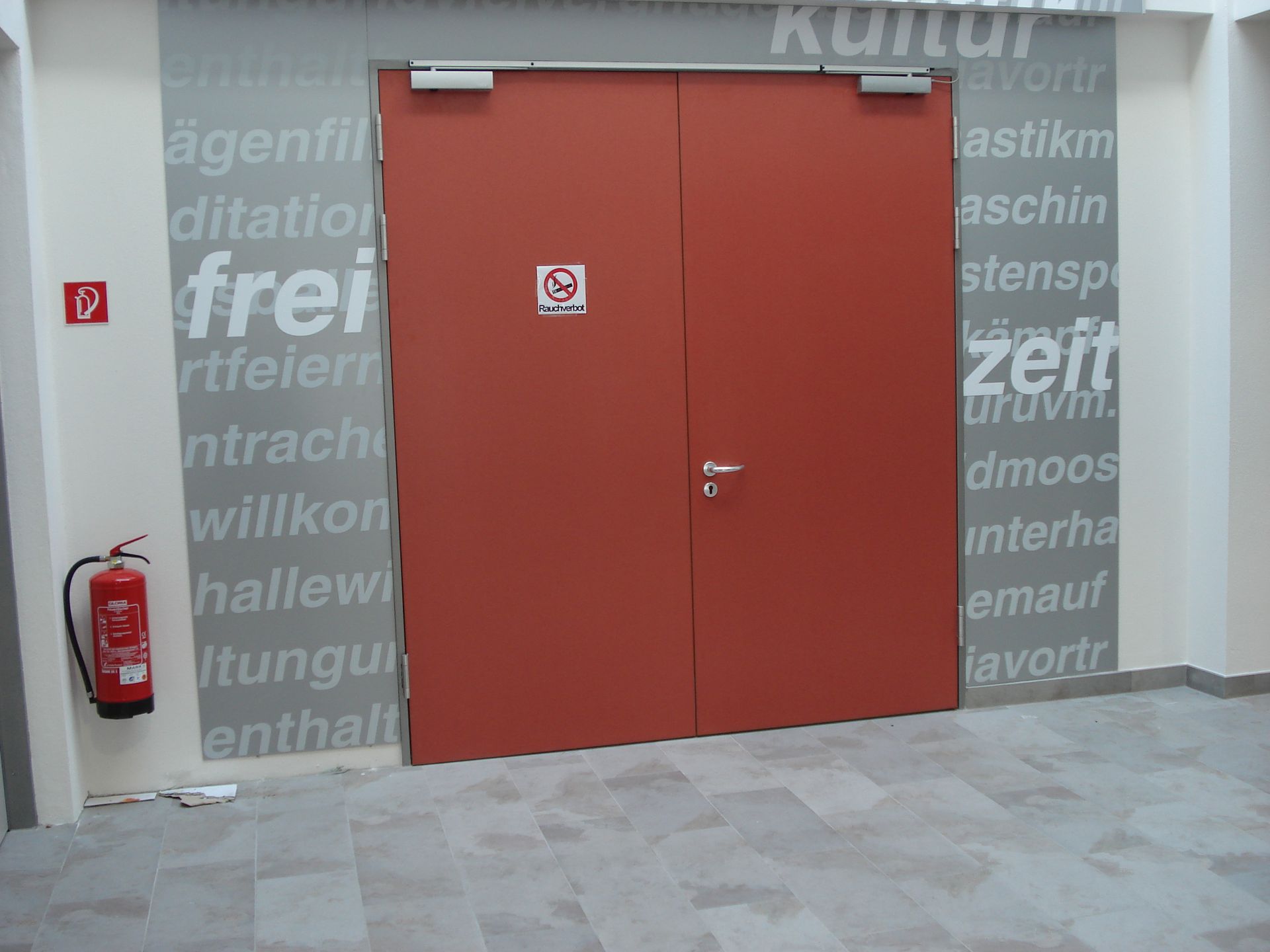 Rote Doppeltüren mit Rauchverbotsschild, Feuerlöscher an der Wand, Texthintergrund.