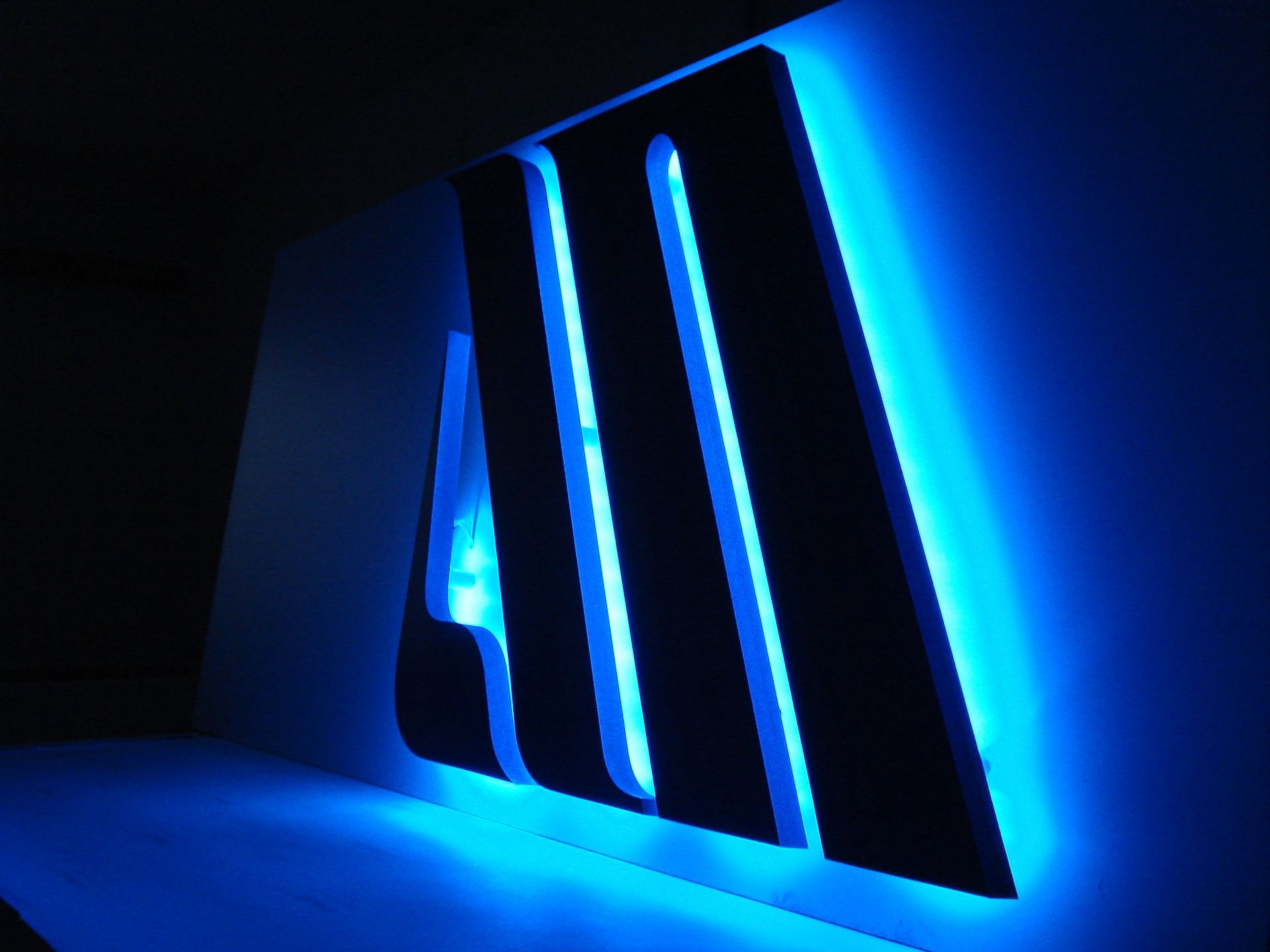 Blau hinterleuchtetes Logo an einer Wand, mit den Buchstaben „AM“ in Schwarz, leuchtend blaue Ränder.