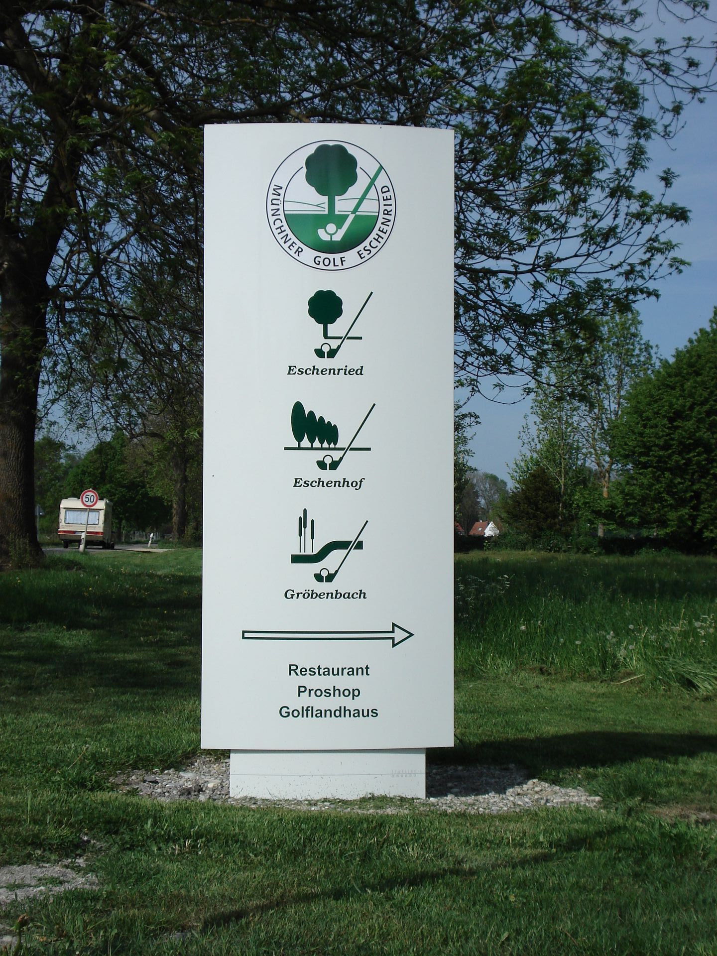 Weißes Schild mit Golfplatz-Logo, Pfeilen und Symbolen, das auf ein Restaurant zeigt.