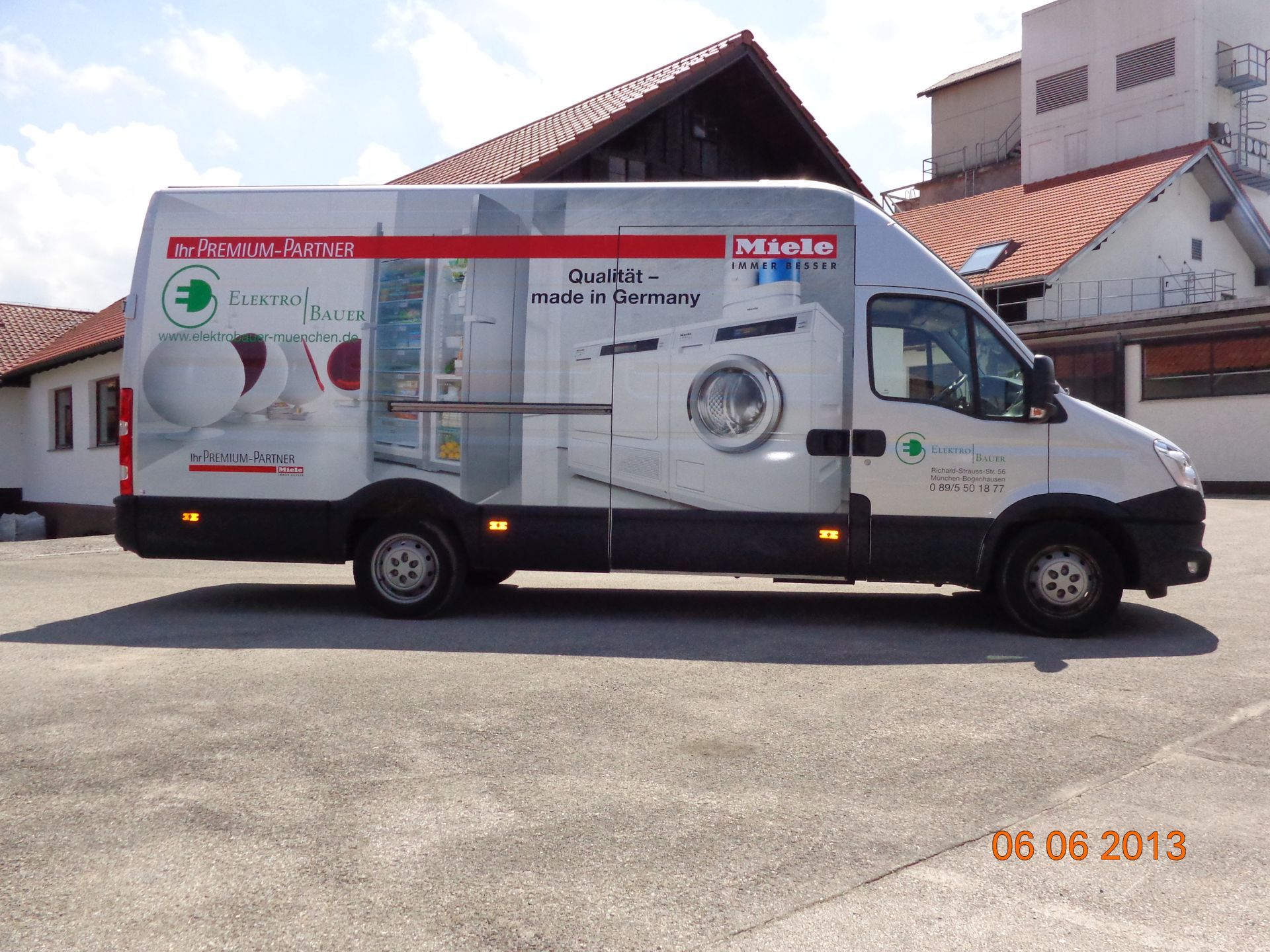 Silberner Lieferwagen mit Miele-Gerätewerbung vor einem Gebäude.