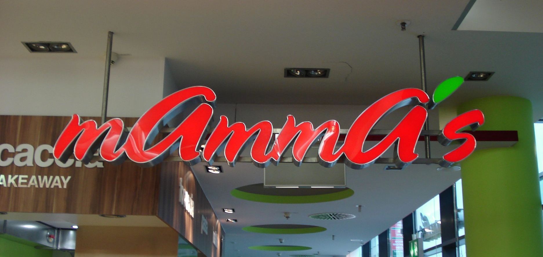 „Mamma‘s“-Restaurantschild, rote Leuchtbuchstaben mit grünem Blattakzent in Einkaufszentrum.