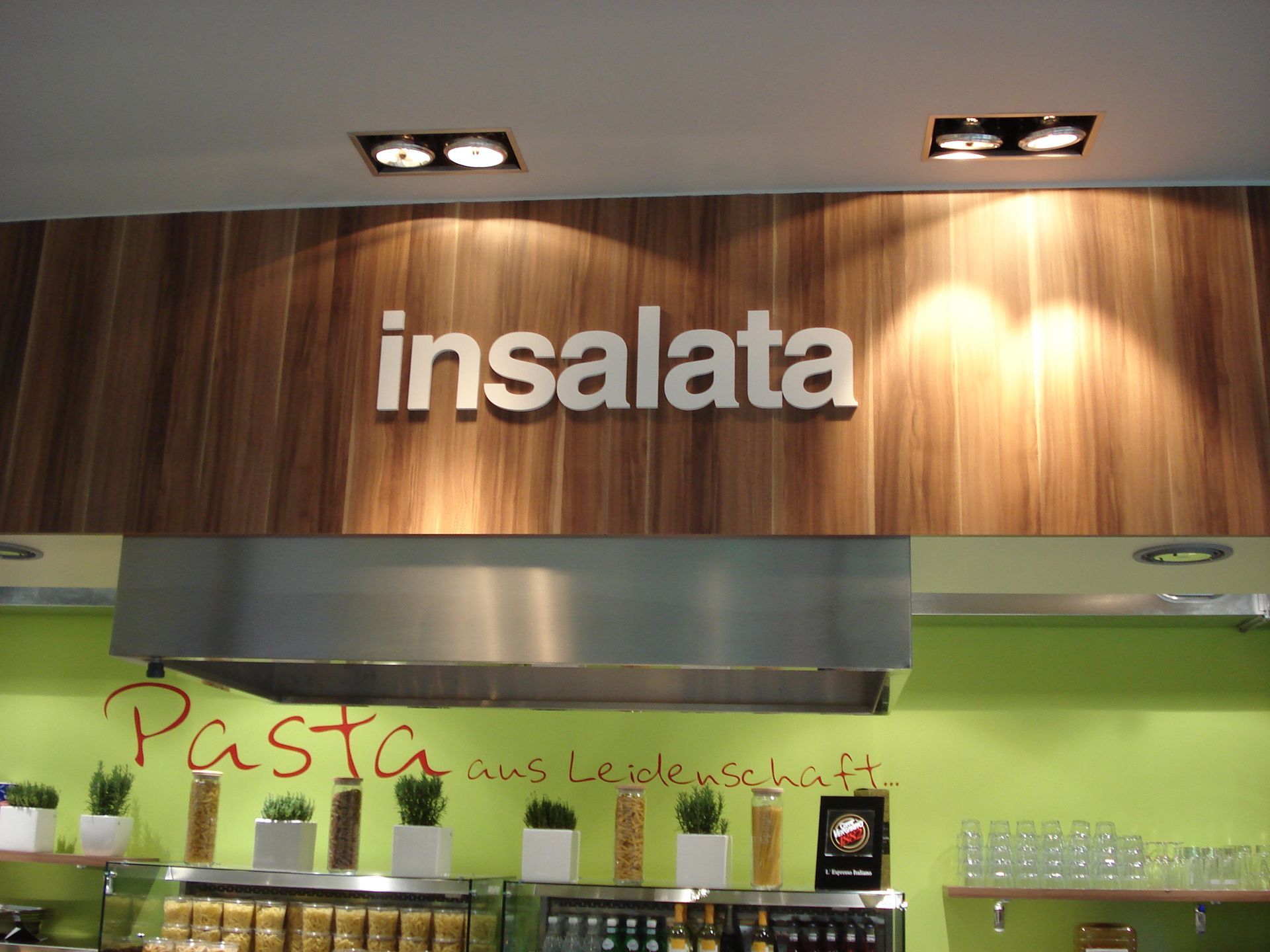 „Insalata“-Schild über einem Bereich zur Essenszubereitung mit grüner Wand und Holzvertäfelung.“