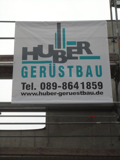 Schild für Huber Gerüstbau, weißer Hintergrund, Logo und Kontaktinformationen, auf Gerüst.
