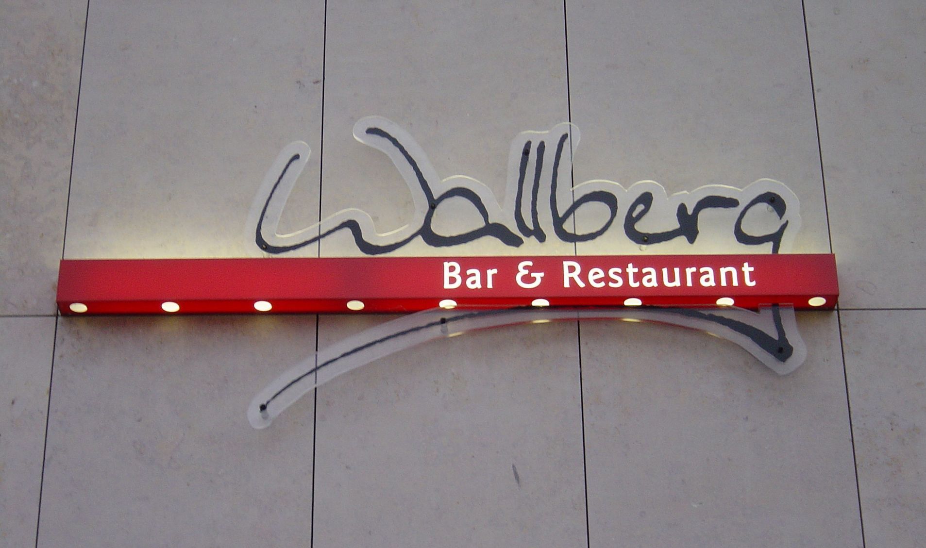 „Wallberg Bar & Restaurant-Schild mit rotem rechteckigen Sockel und leuchtenden Buchstaben.