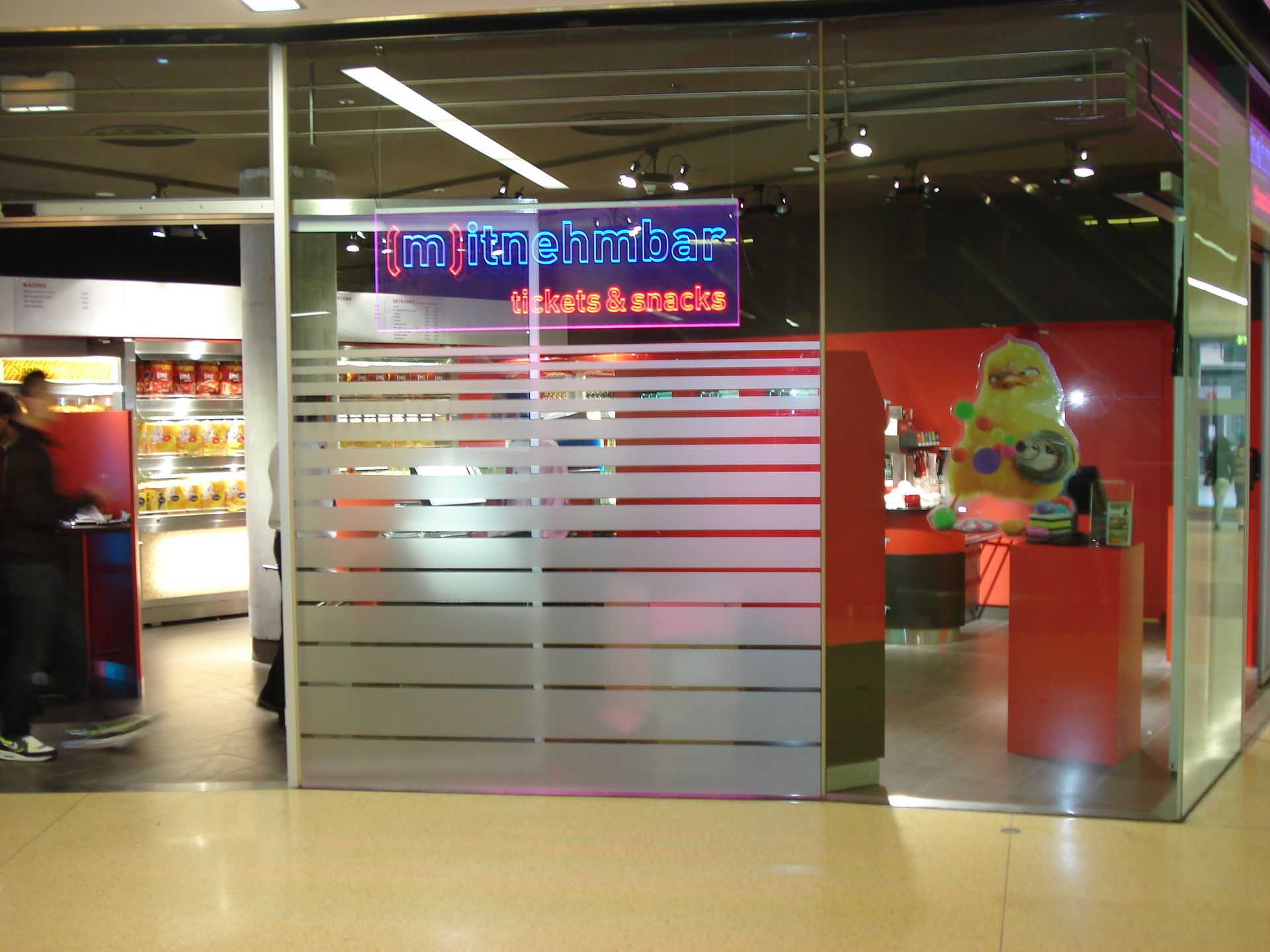 Ein Ticketschalter in einem Einkaufszentrum mit Milchglasfenster, Neonreklame und Plüschtieren.