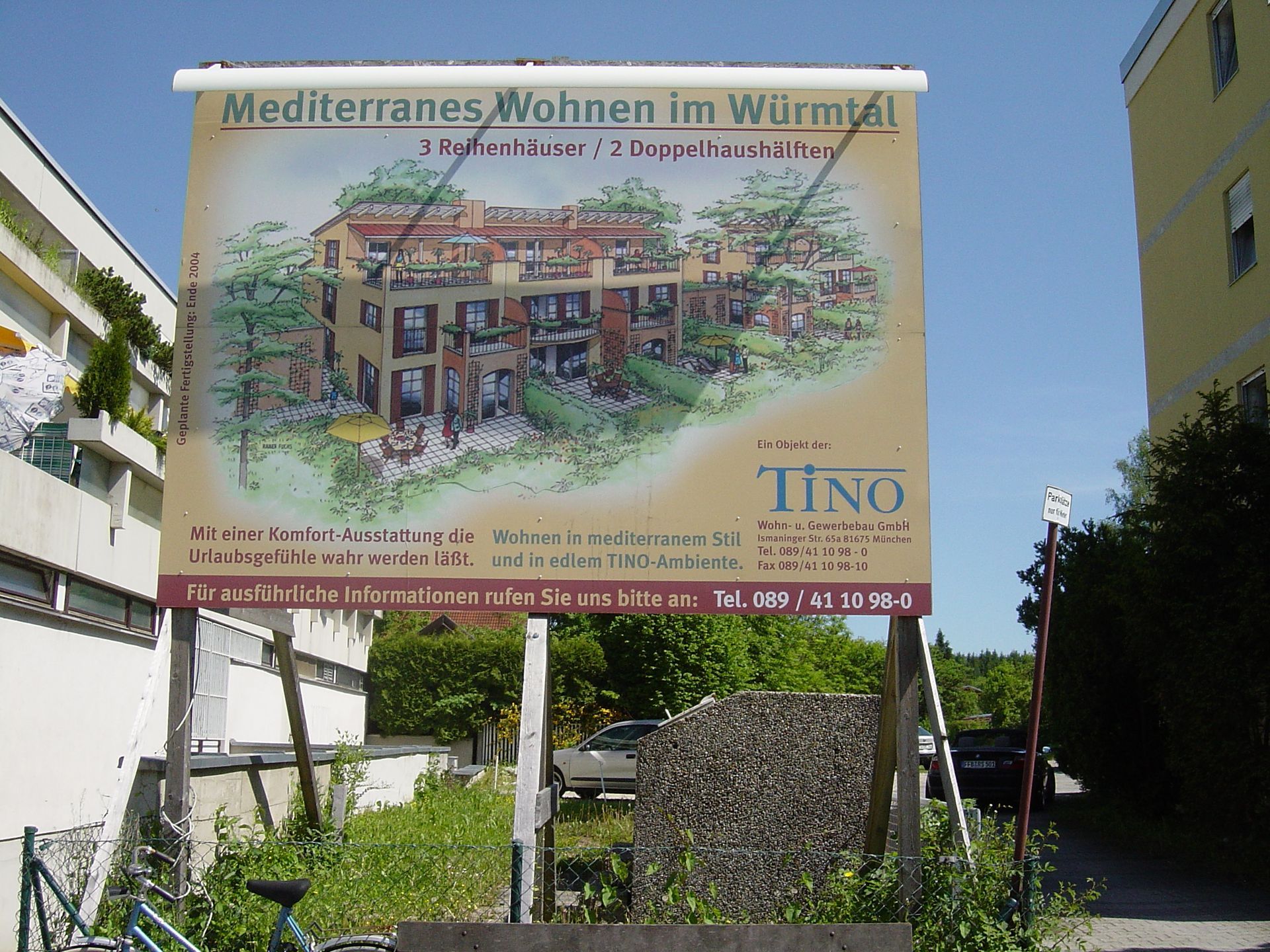 Werbetafel für Wohnungen im mediterranen Stil im Wurmtal mit Abbildung des Gebäudes; sonniger Tag.