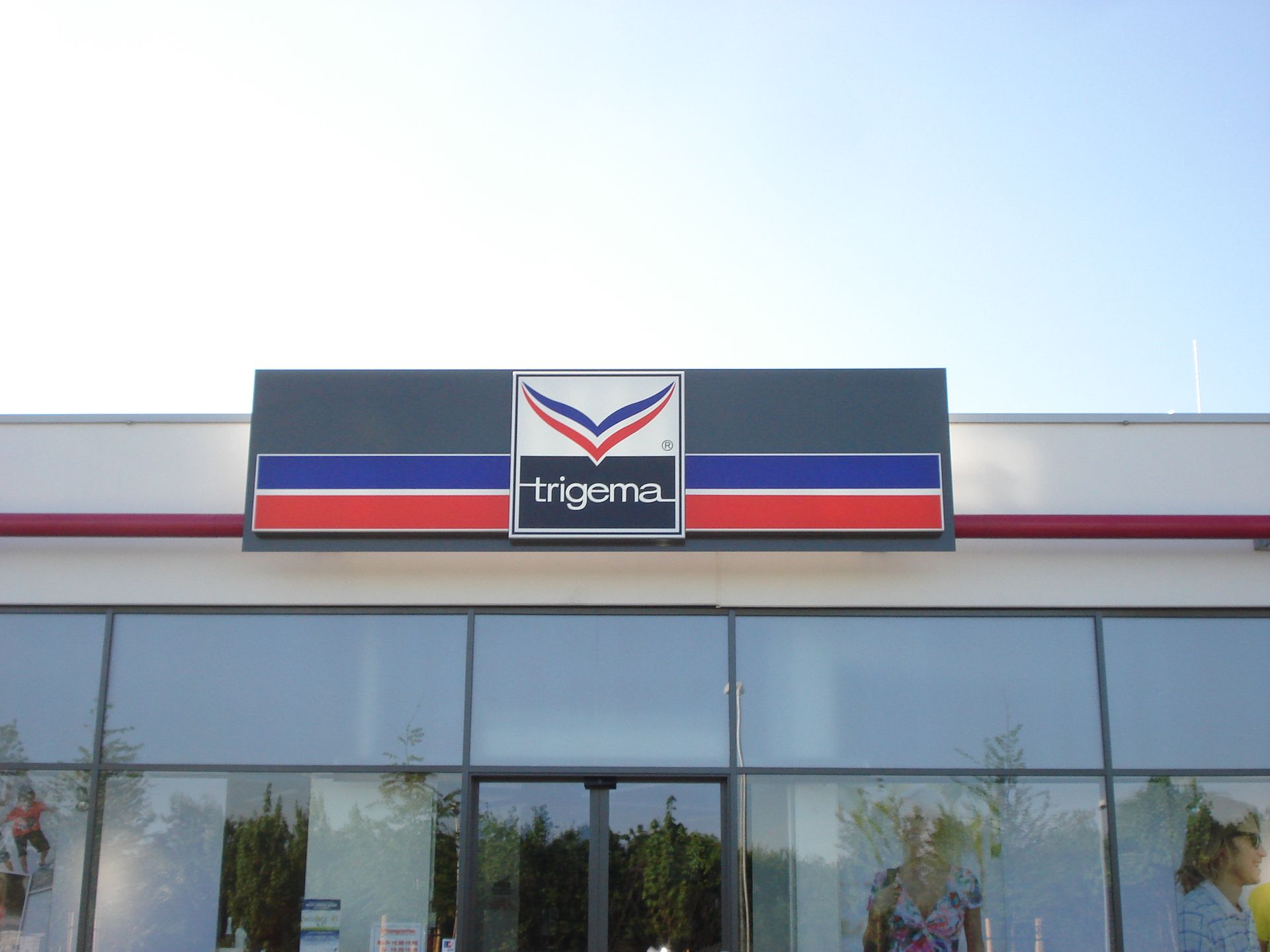 Leuchtkasten „Trigana“ über dem Eingang eines Geschäfts.