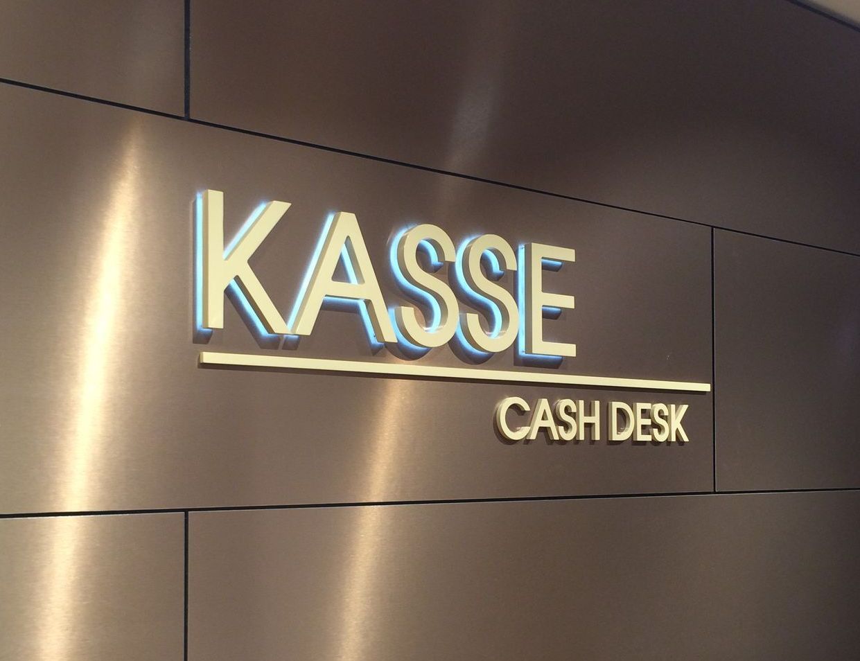 Leuchtbuchstaben „KASSE“ an einer Wand.