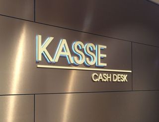 Lichtwerbung mit der Aufschrift „KASSE CASH DESK“ an einer Wand.