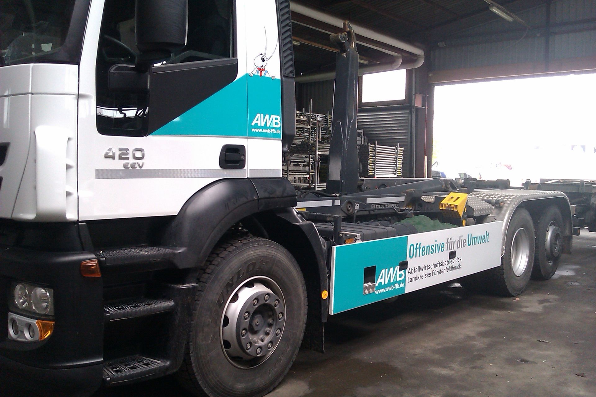Weißer und türkisfarbener AWS-Truck, in einer Garage geparkt. Schwarzer Kotflügel und Reifen.