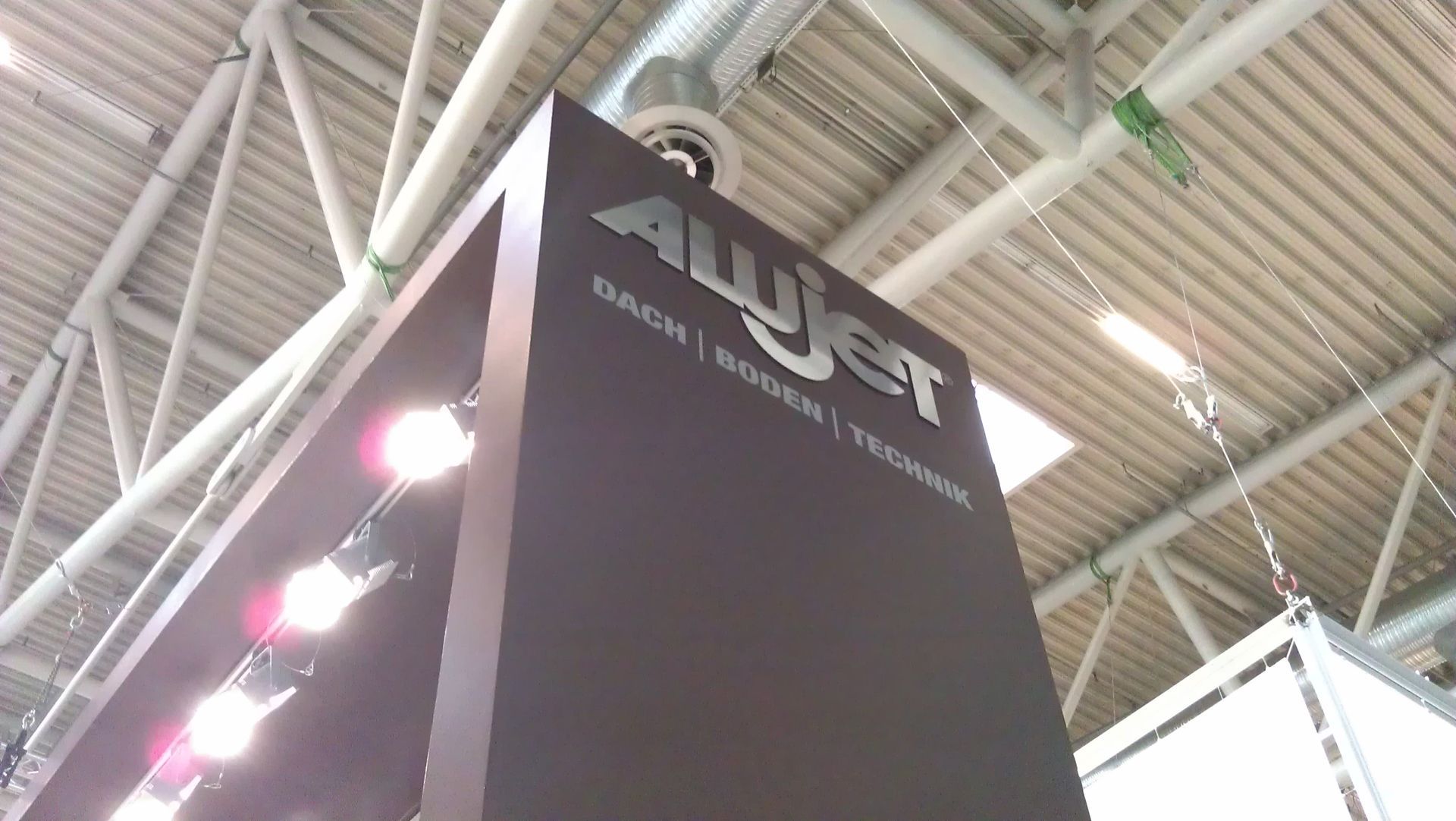 Braunes Schild mit „AWjet“-Logo und den Worten „BAD“, „BODEN“ und „TECHNIK“ unter einer weißen Decke mit Lichtern.