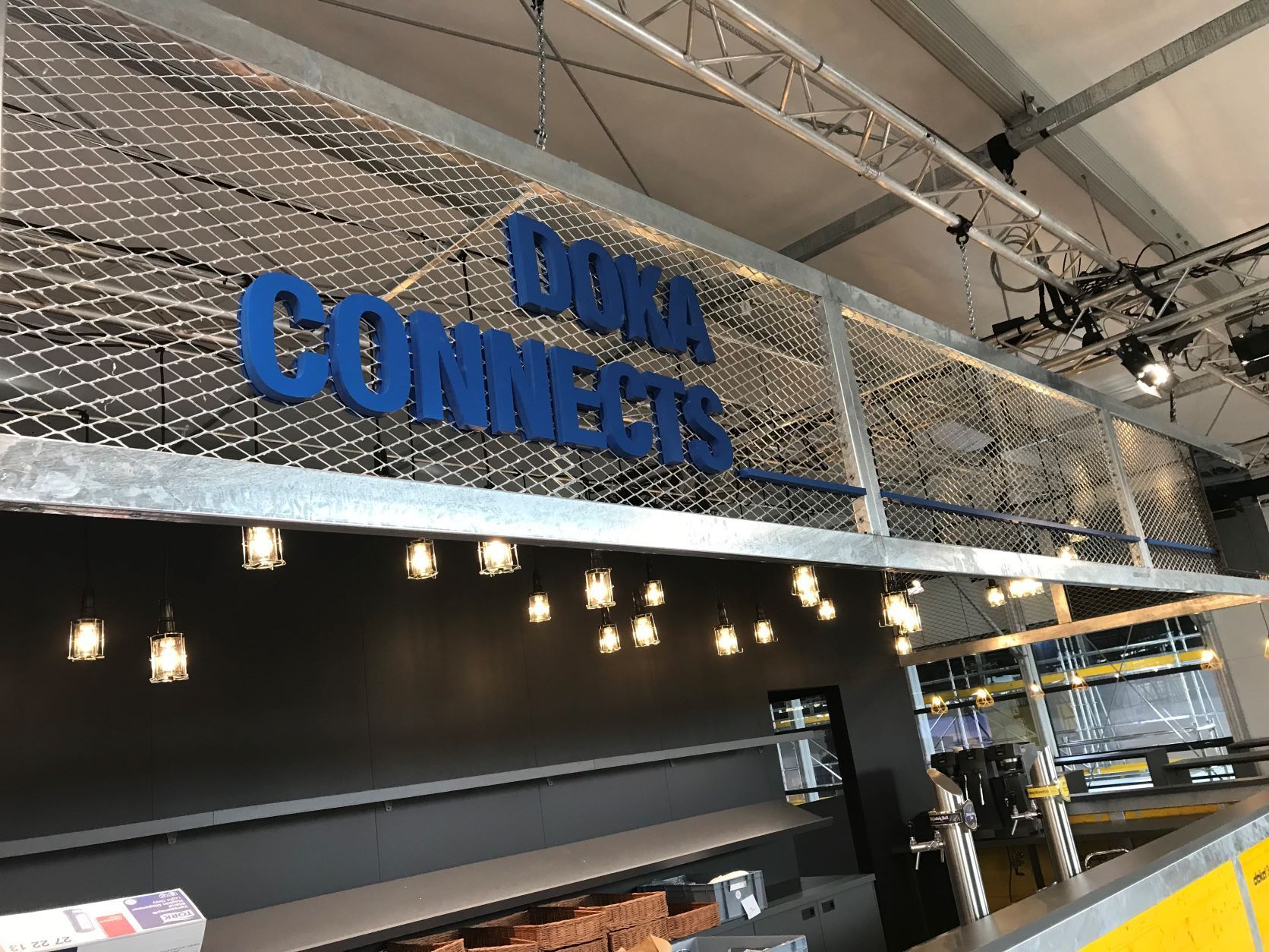 „Deka Connects“-Schild in blauen Buchstaben, über einer Bar mit Lichterketten, in modernem Ambiente.