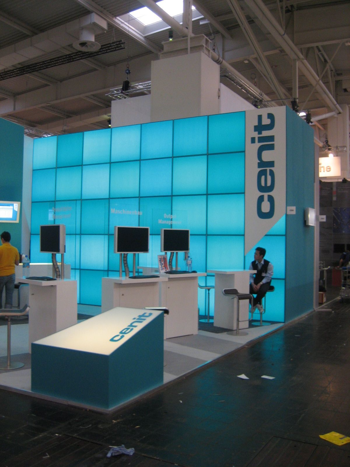 Ein Messestand, beleuchtet mit blauen Quadraten. „Cenit“-Logo an der Wand. Menschen an Computern.