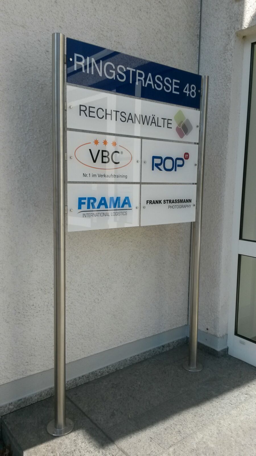 Wegweiser zur Ringstraße 48 mit Büronamen und Logos auf weißen Tafeln.