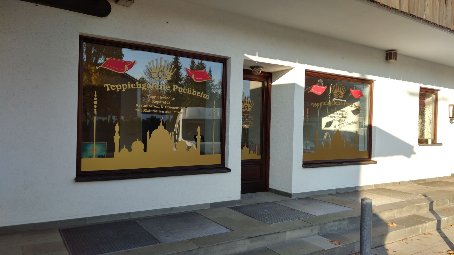 Schaufenster mit goldenen und roten Grafiken und Texten in den Fenstern; weißes Gebäude.