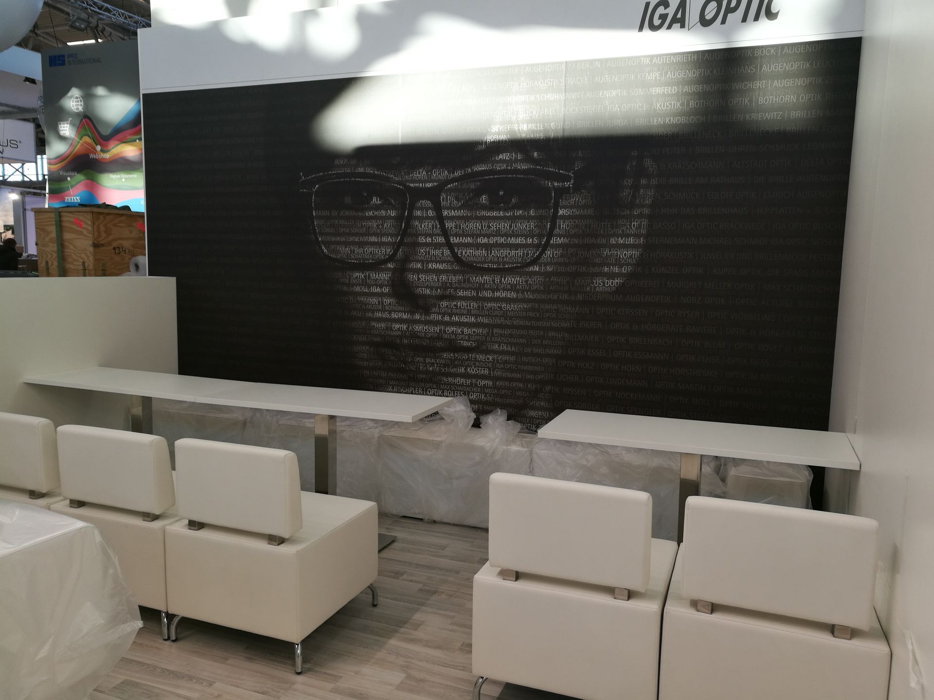 Ein Display mit einem Gesicht aus Buchstaben, darunter weiße Bänke und Stühle in einem hellen Raum.