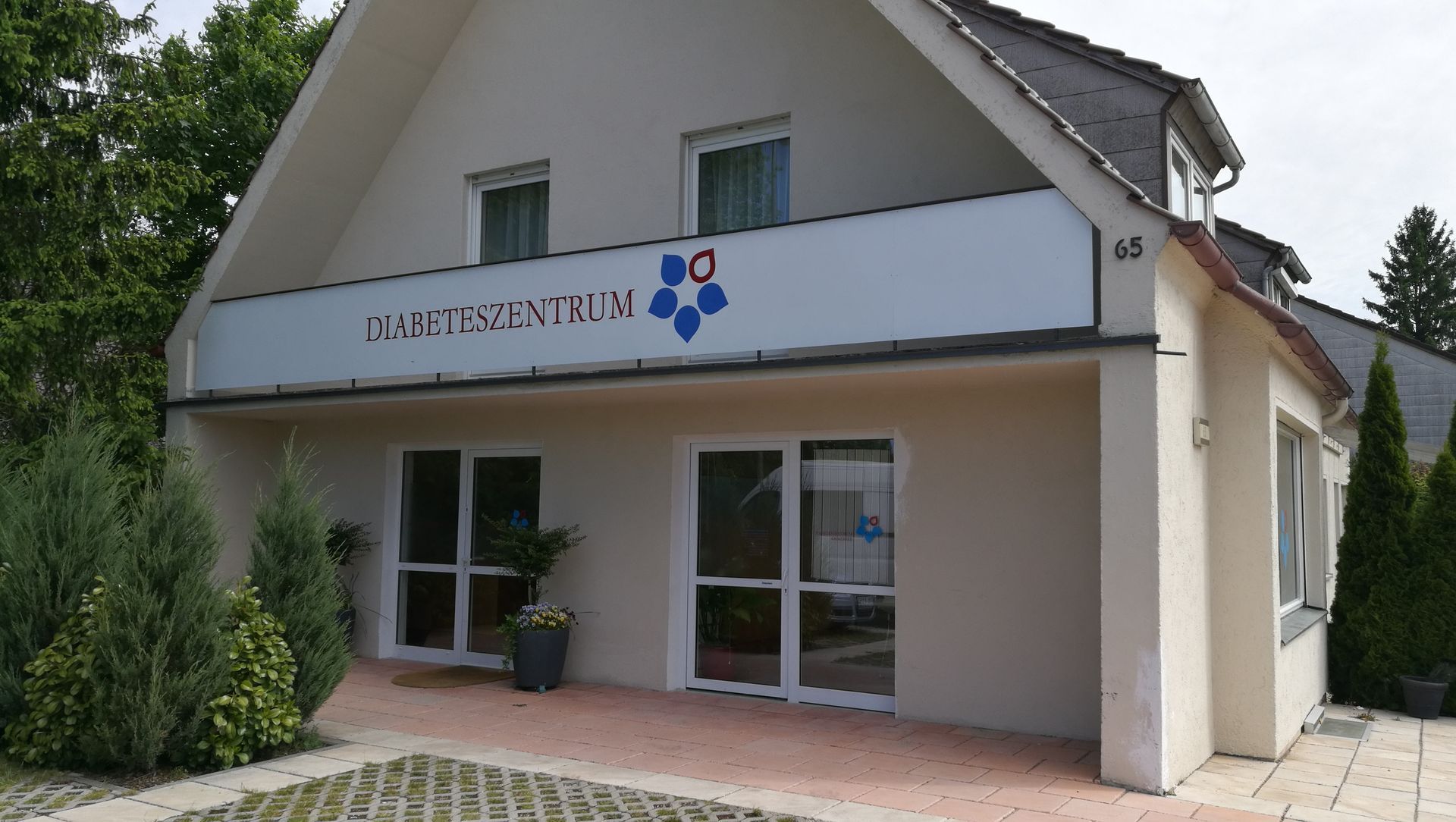 Ein helles Gebäude mit einem Schild mit der Aufschrift „Gesundheitszentrum“ und einem blauen Blumenlogo.