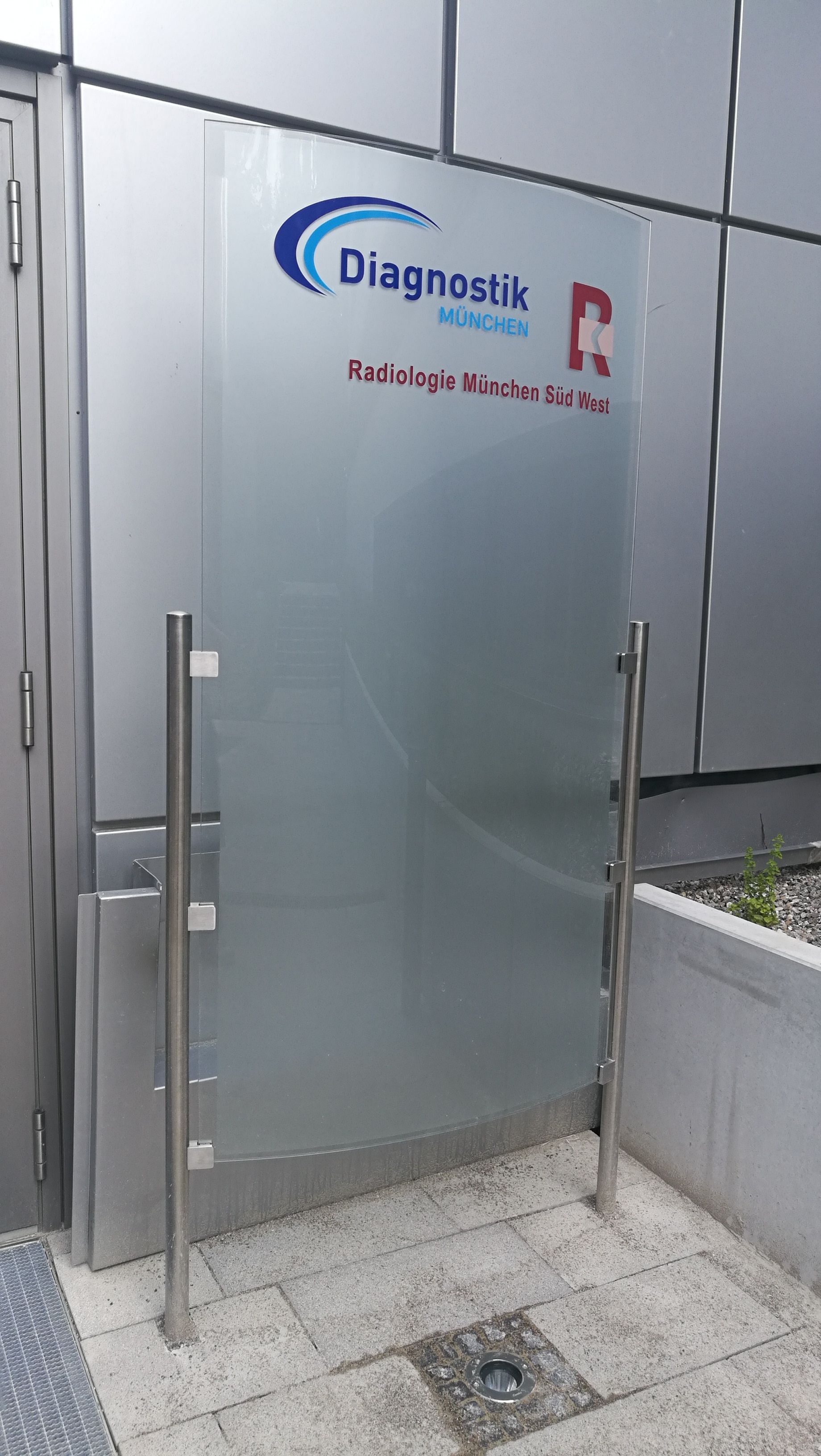 Milchglastür mit „Diagnostik“-Logo und Schriftzug vor einem Gebäude.