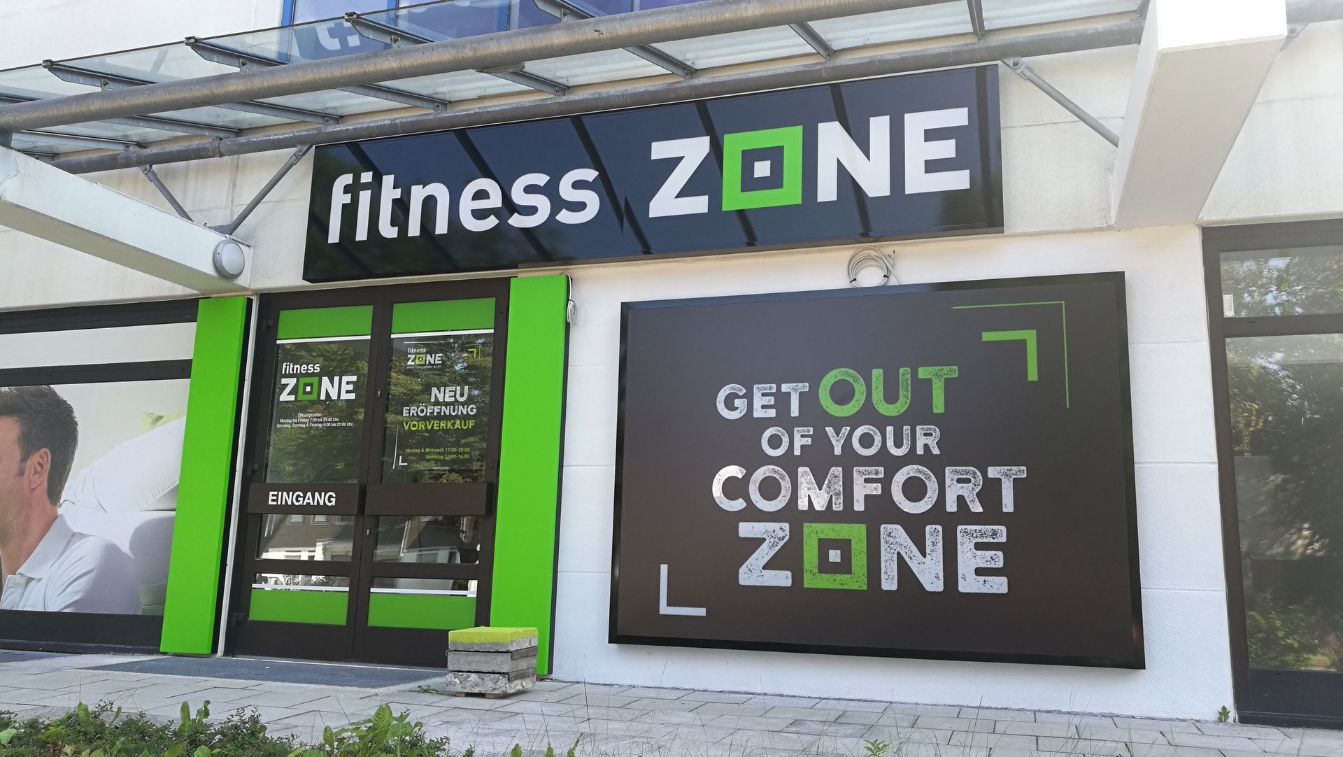 Eingang zum Fitnessstudio Fitness Zone mit schwarz-grüner Beschilderung und Leuchtkasten.