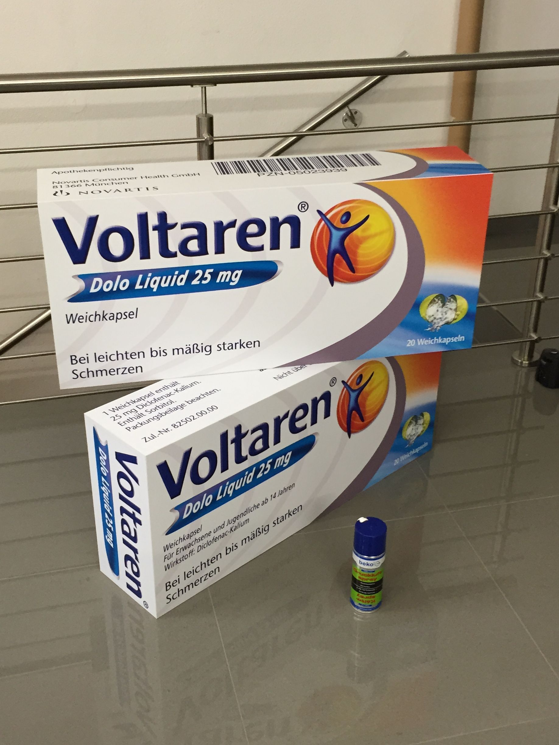 Schachteln mit Schmerzmitteln von Voltaren und einer kleinen Sprühflasche auf einer reflektierenden Oberfläche.