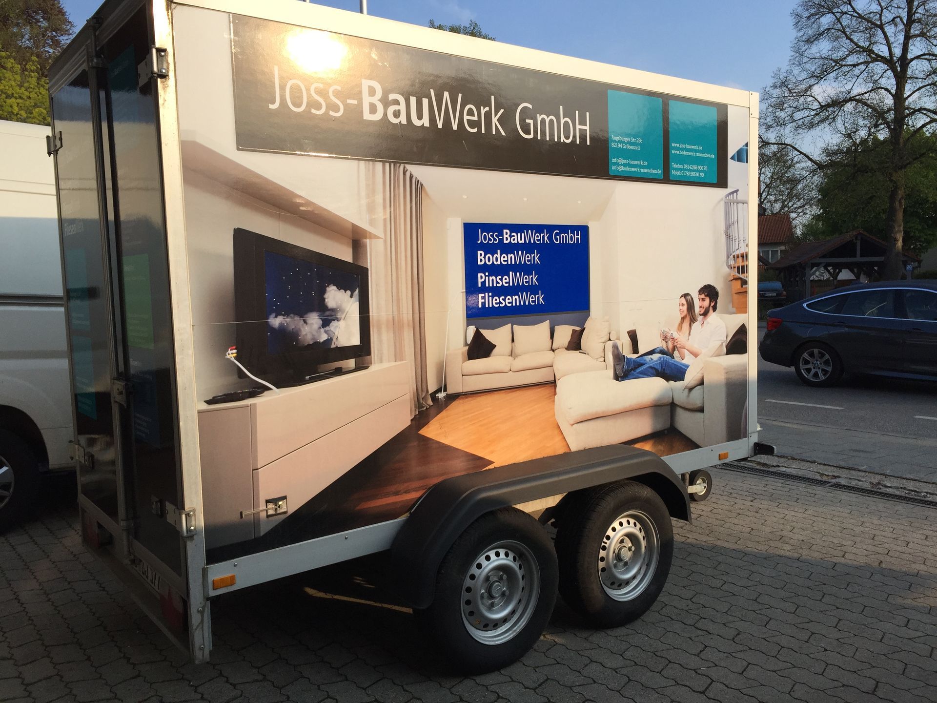 Trailer mit Werbung für die Joss-BauWerk GmbH, der ein Wohnzimmer mit Fernseher und einem Paar zeigt.