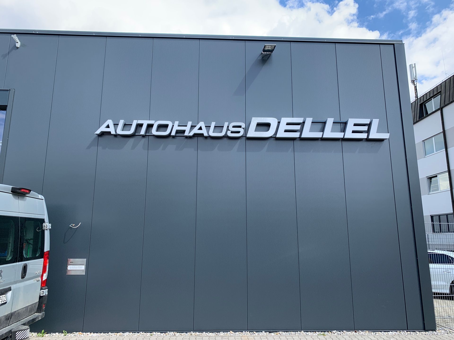 Graues Gebäude mit dem Schild „Autohaus Dellel“. Weiße Buchstaben auf einer strukturierten Wand, Außenansicht.