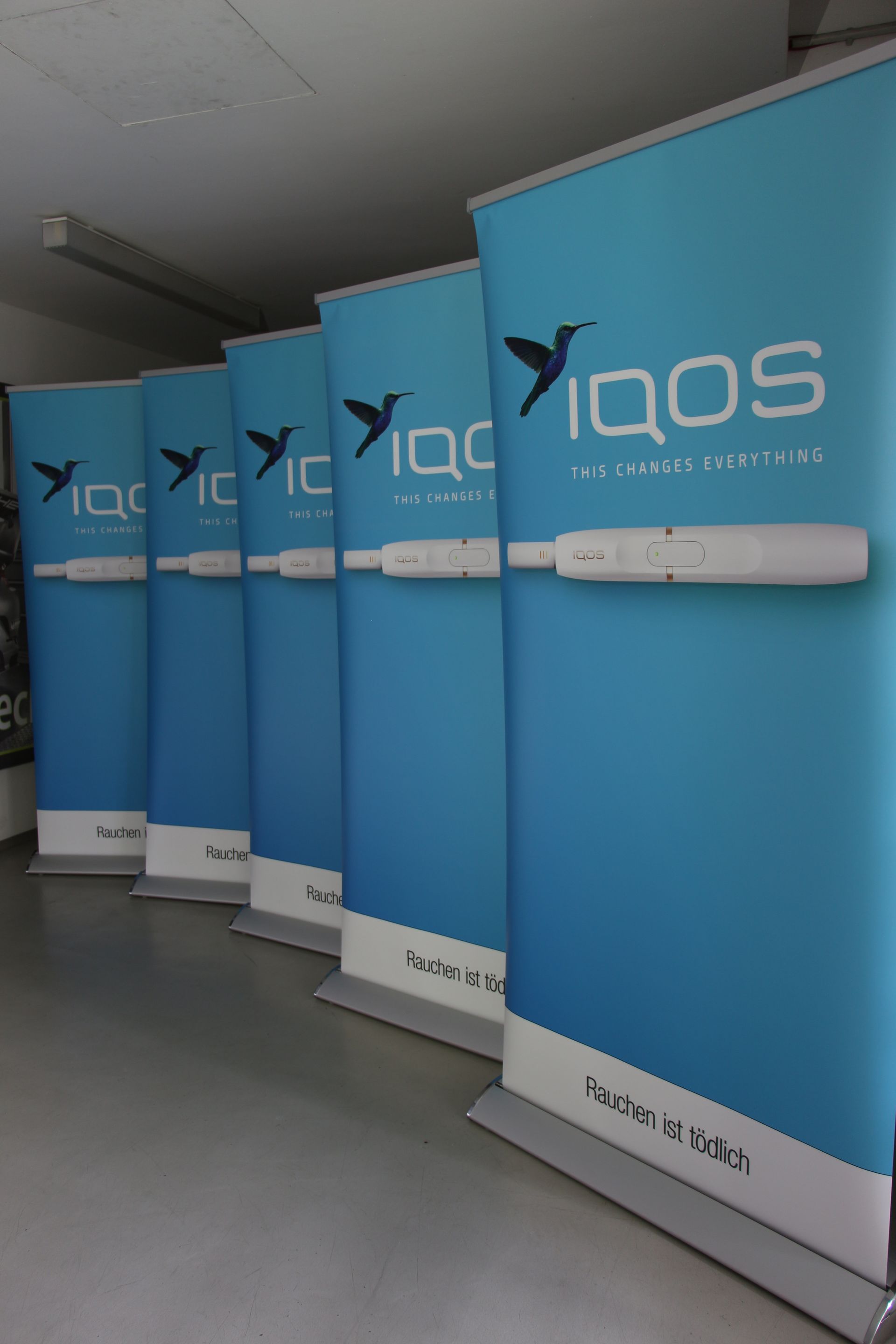 Blaue IQOS-Werbebanner mit einem Kolibri-Logo in einem Geschäft.