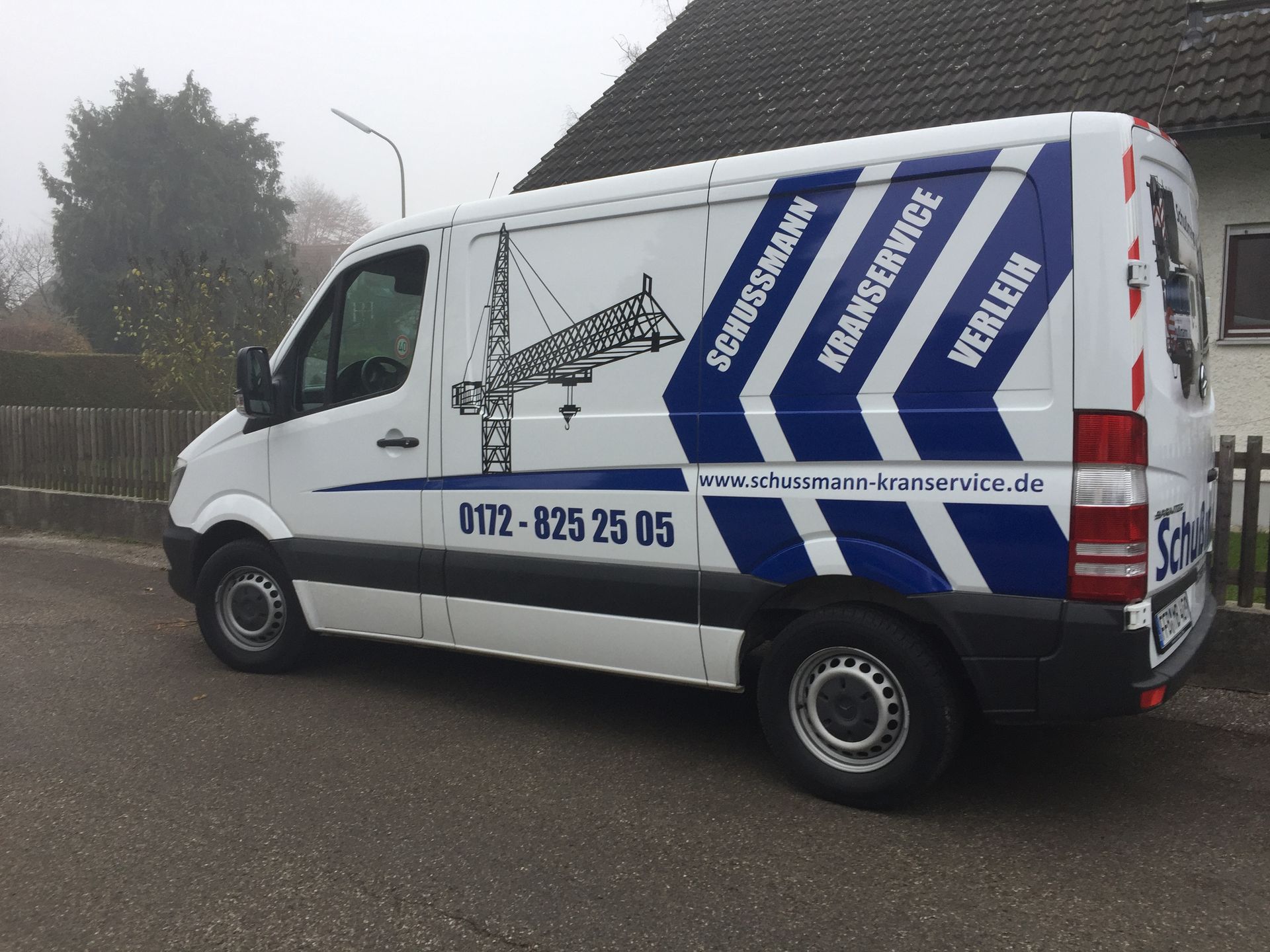 Weißer Transporter mit blauen Streifen und Kranlogo. Auf der Seite steht „Burgessmann Kranservice“.