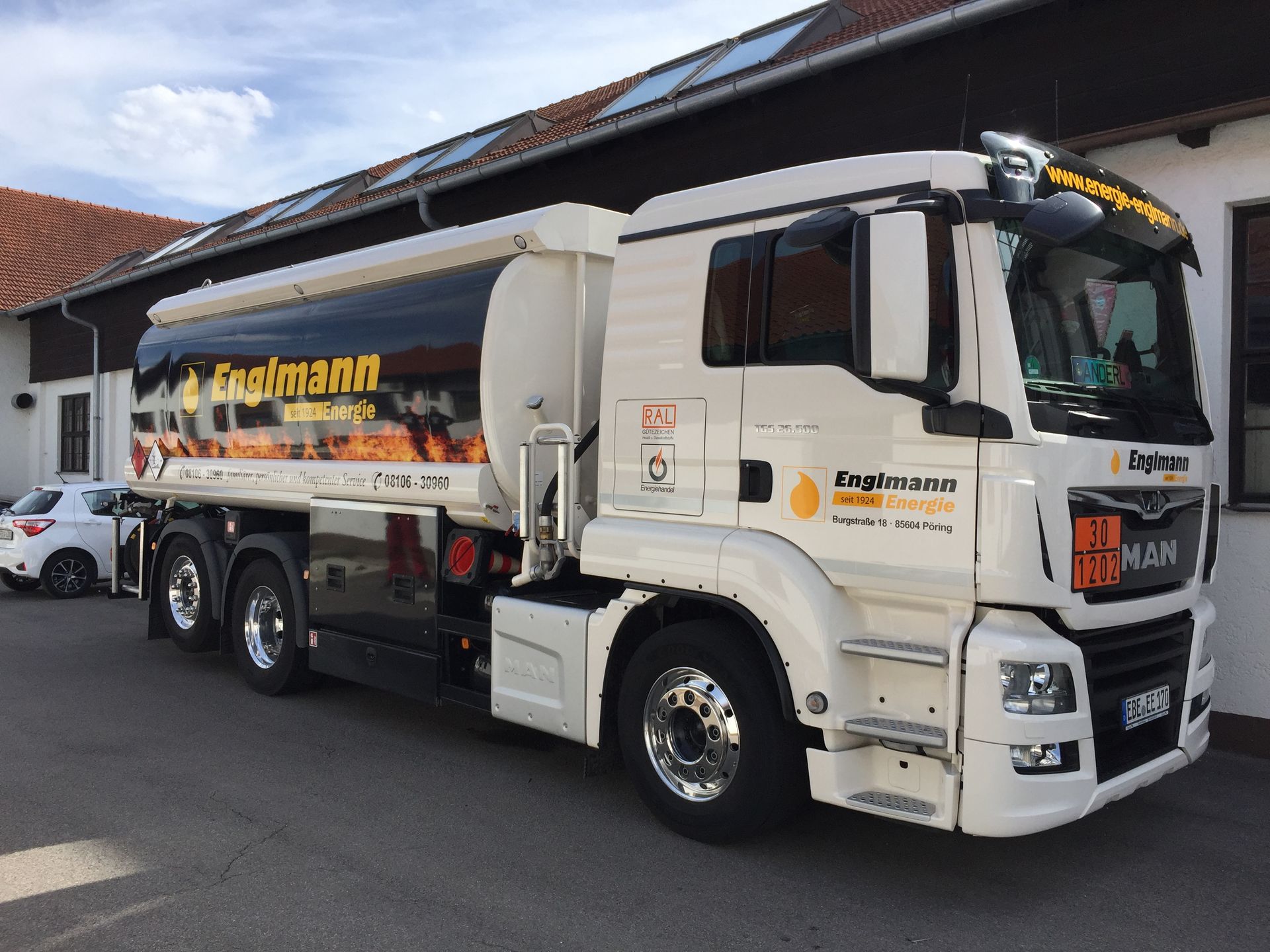Weißer Tankwagen mit schwarzem Tank und „Englmann“-Logo, vor dem Gebäude geparkt.