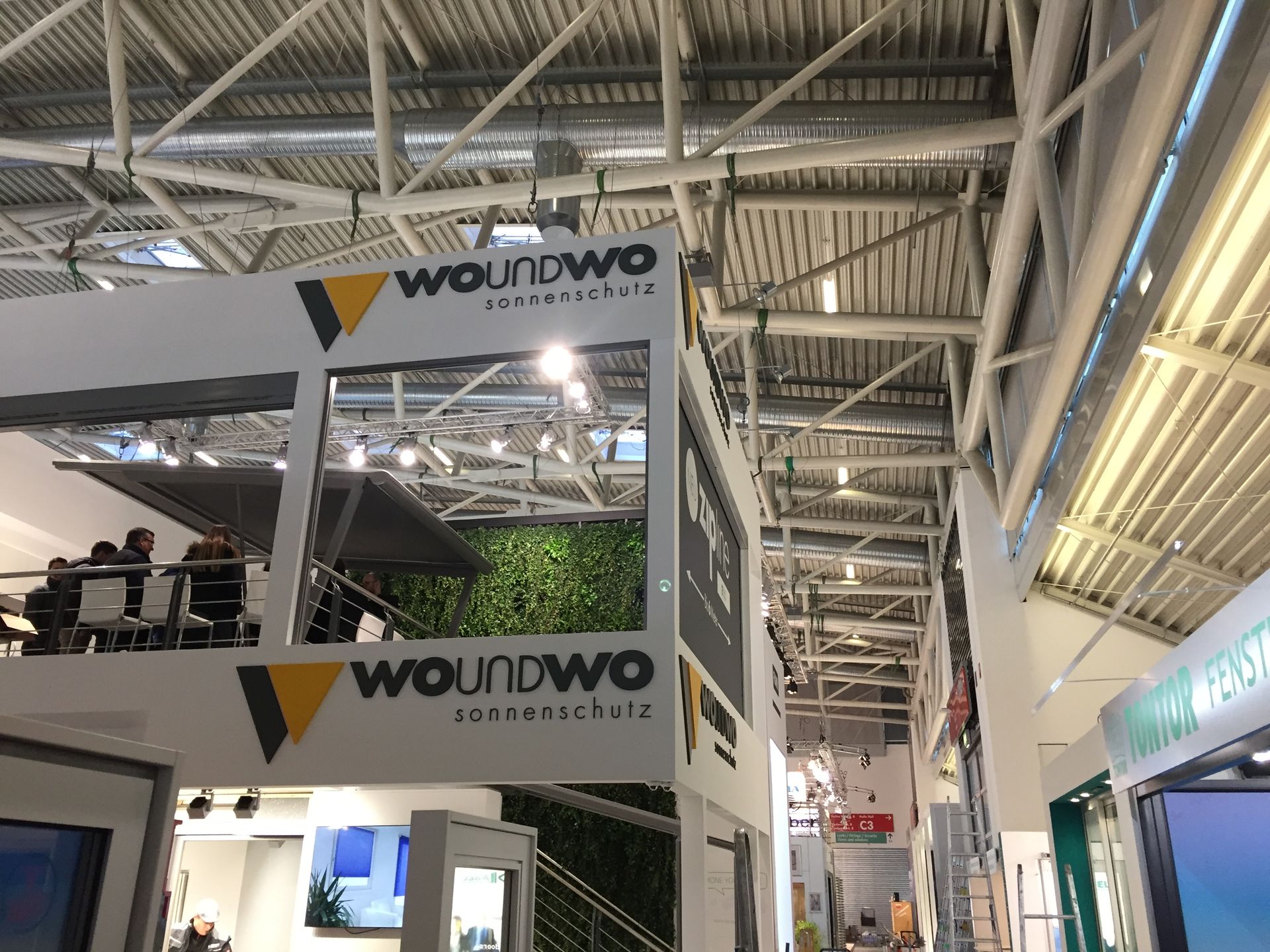 Mehrstöckiger Messestand mit „woundwo“-Beschilderung und Begrünung.