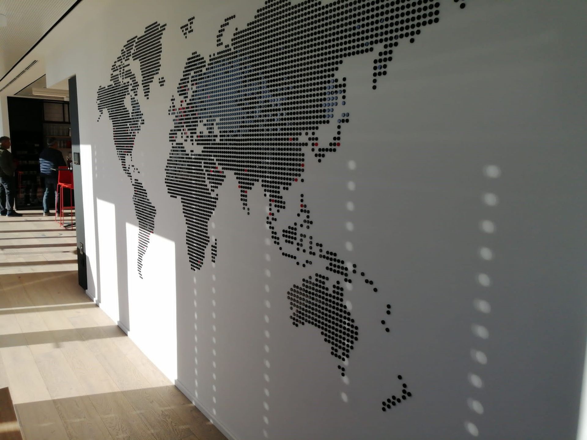 Schwarz-weiße Weltkarte aus Punkten auf einer weißen Wand in einem Flur. Sonnenlicht erzeugt Schatten.