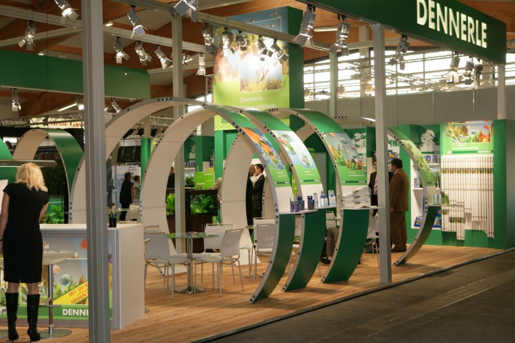 Messestand mit geschwungenen Bögen, grün-weißem Branding und Menschen.