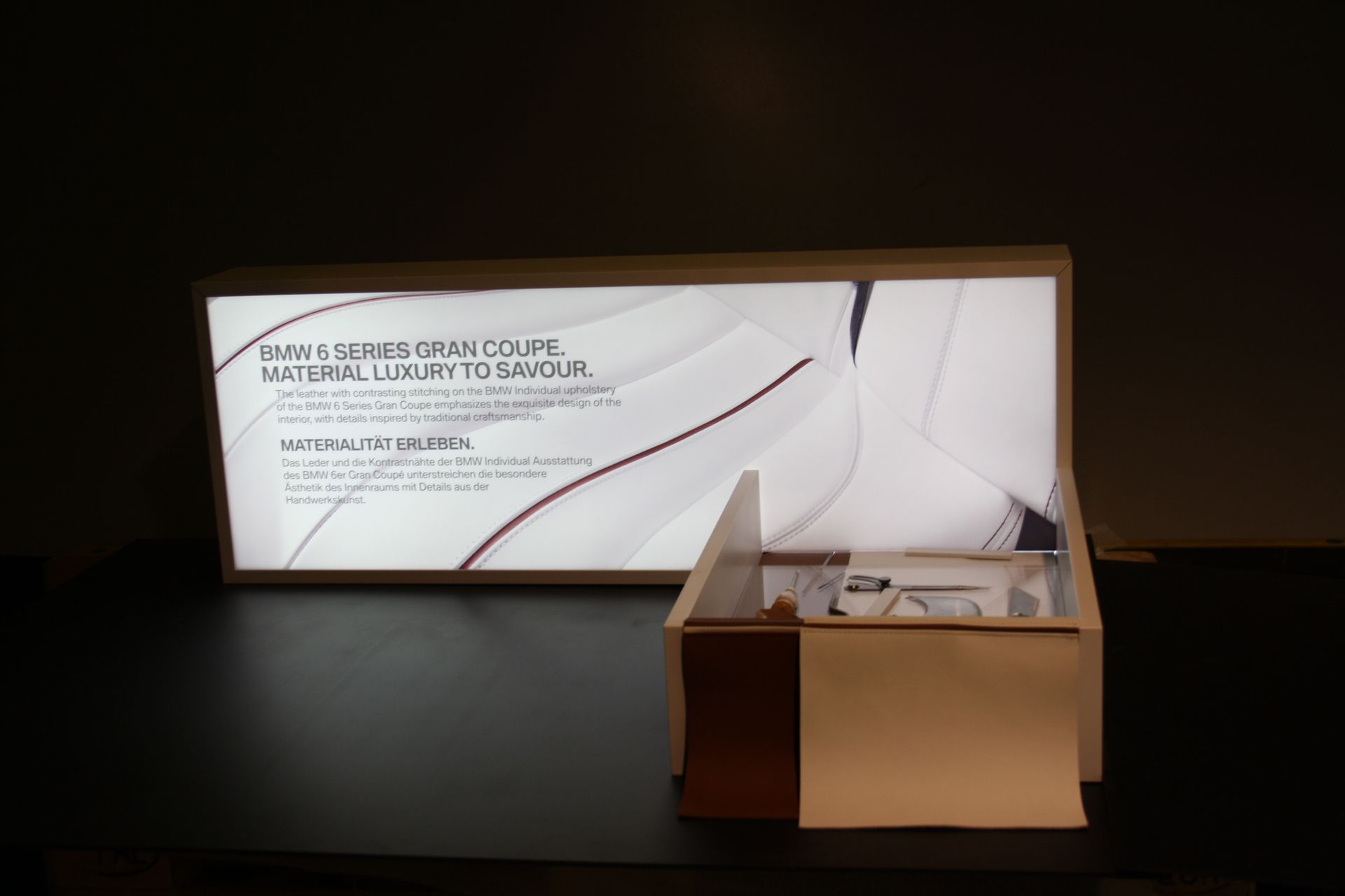 Vitrine mit Leuchtreklame, Kiste mit Objekten auf schwarzem Untergrund.