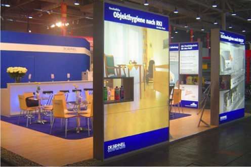 Ein Messestand in den Farben Blau und Gelb. Präsentation von Reinigungsprodukten, ein Barbereich mit Stühlen und Tischen.