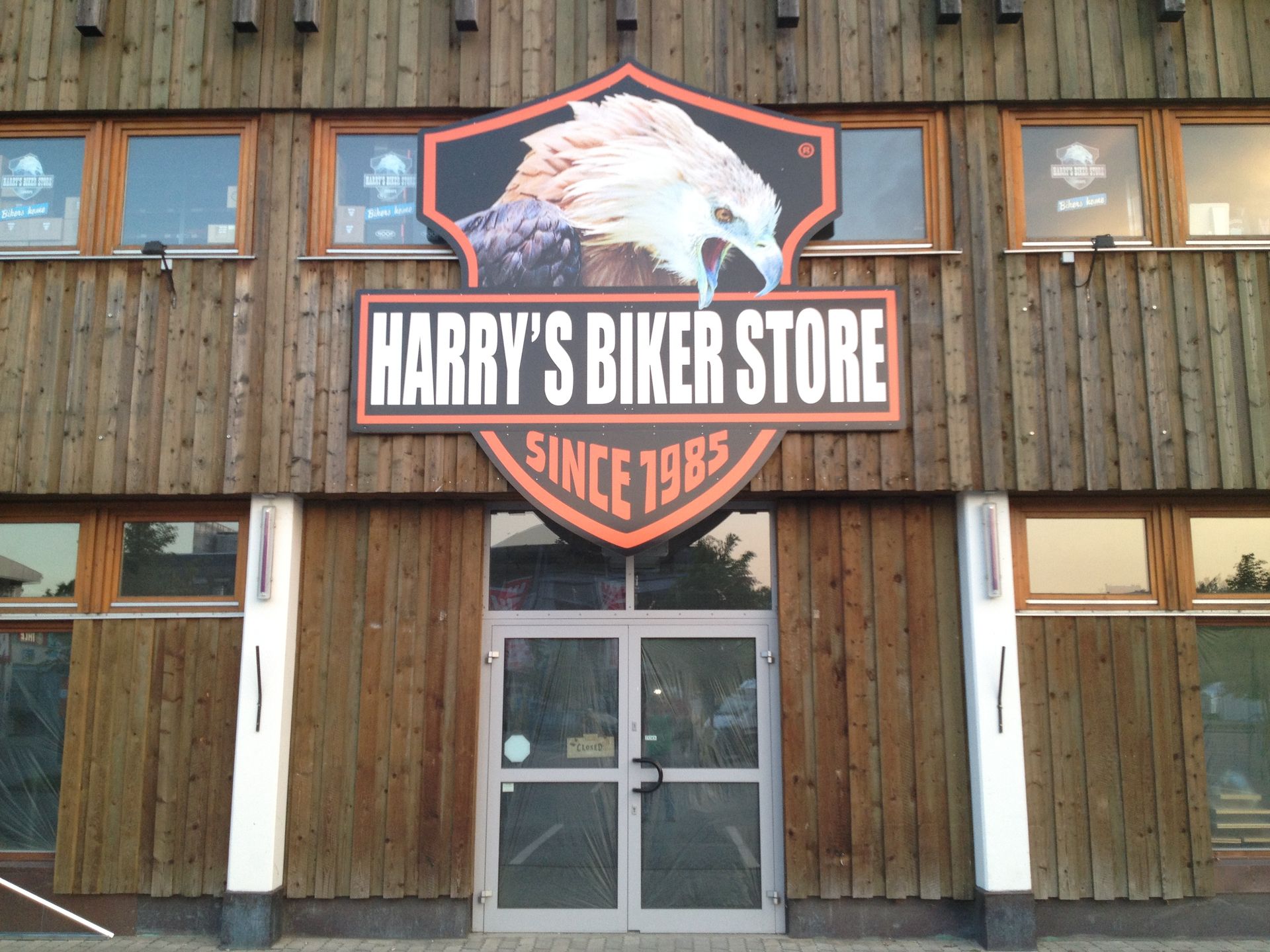Schild von Harry's Biker Store mit Adlergrafik über doppelten Glastüren auf einem Holzgebäude. „Seit 1985“.