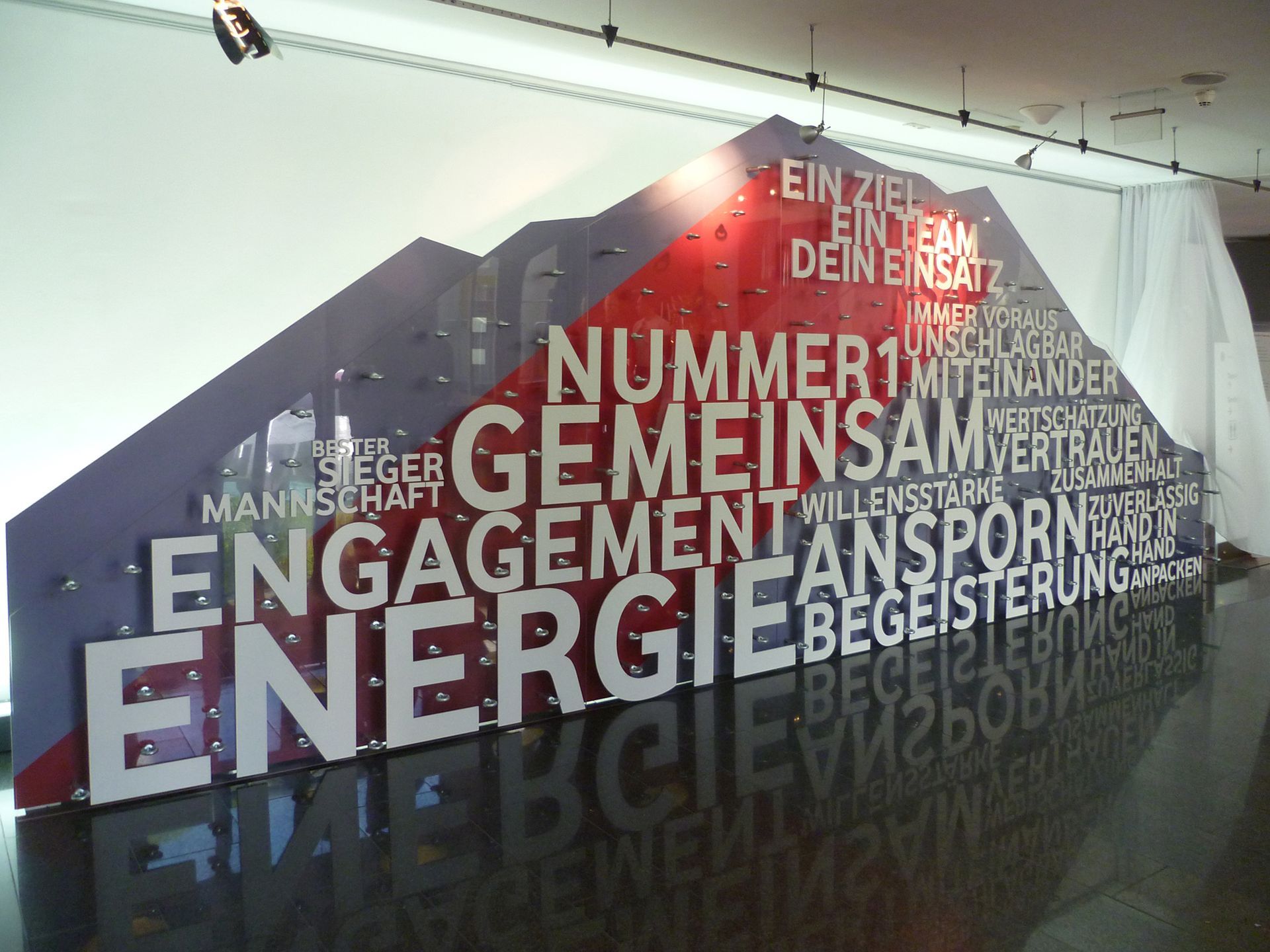 Großes Wandbild mit deutschen Wörtern wie „GEMEINSAM“, „ENGAGEMENT“ und „ENERGIE“.
