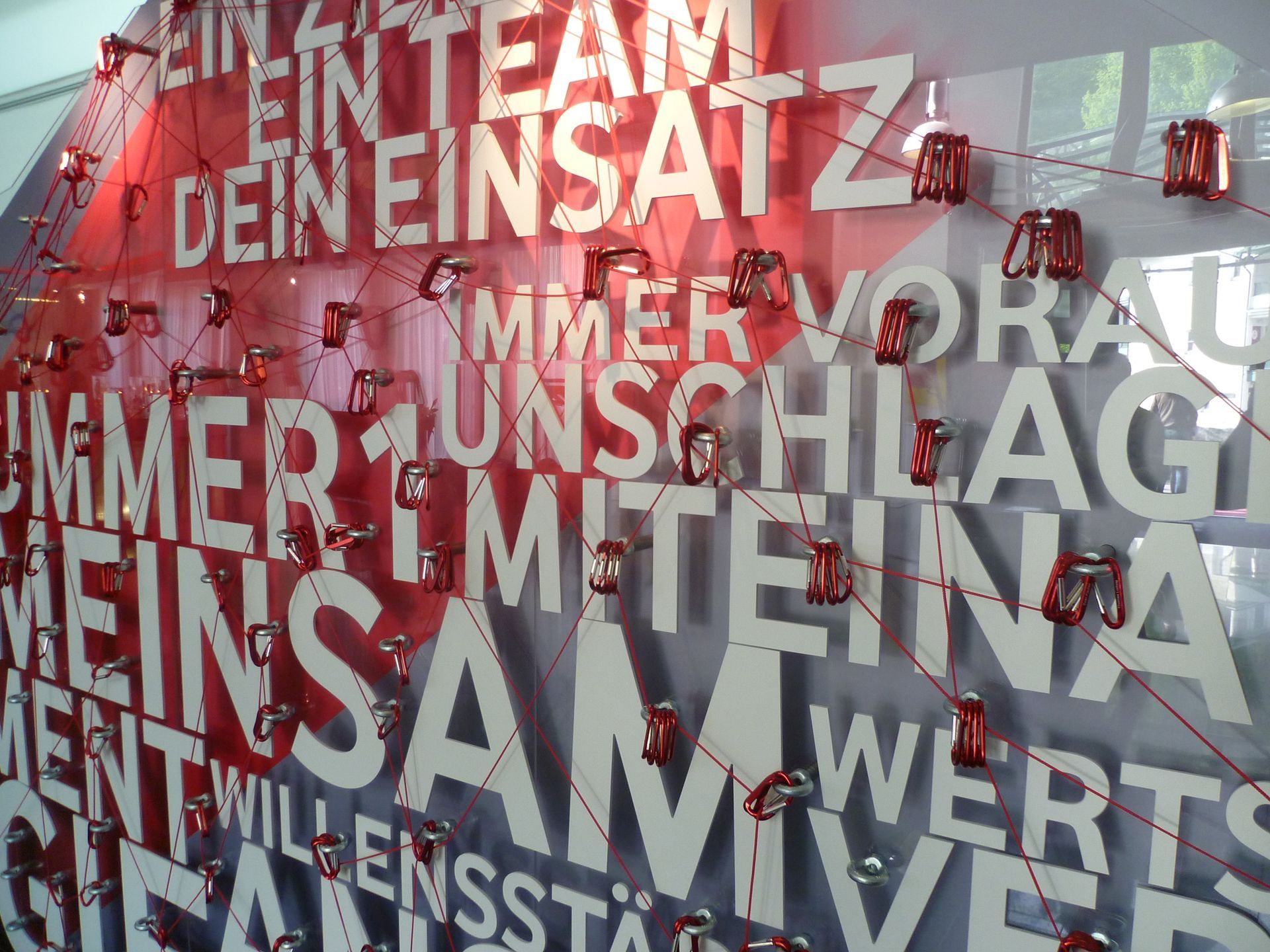 Weißer Text „EIN TEAM DEIN EINSATZ“ mit roter Schnur und Dosen auf weißem Hintergrund.
