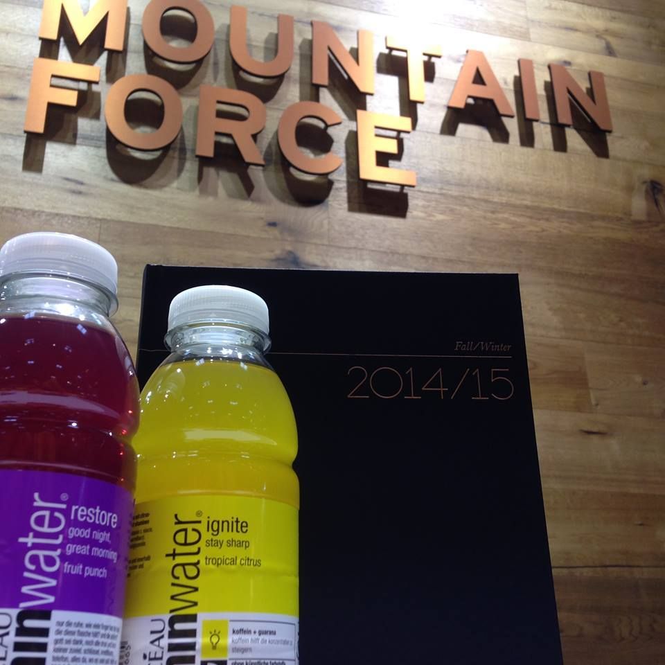 Zwei Flaschen „Regenwasser“-Getränke und ein schwarzer Planer vor einem „Mountain Force“-Schild.