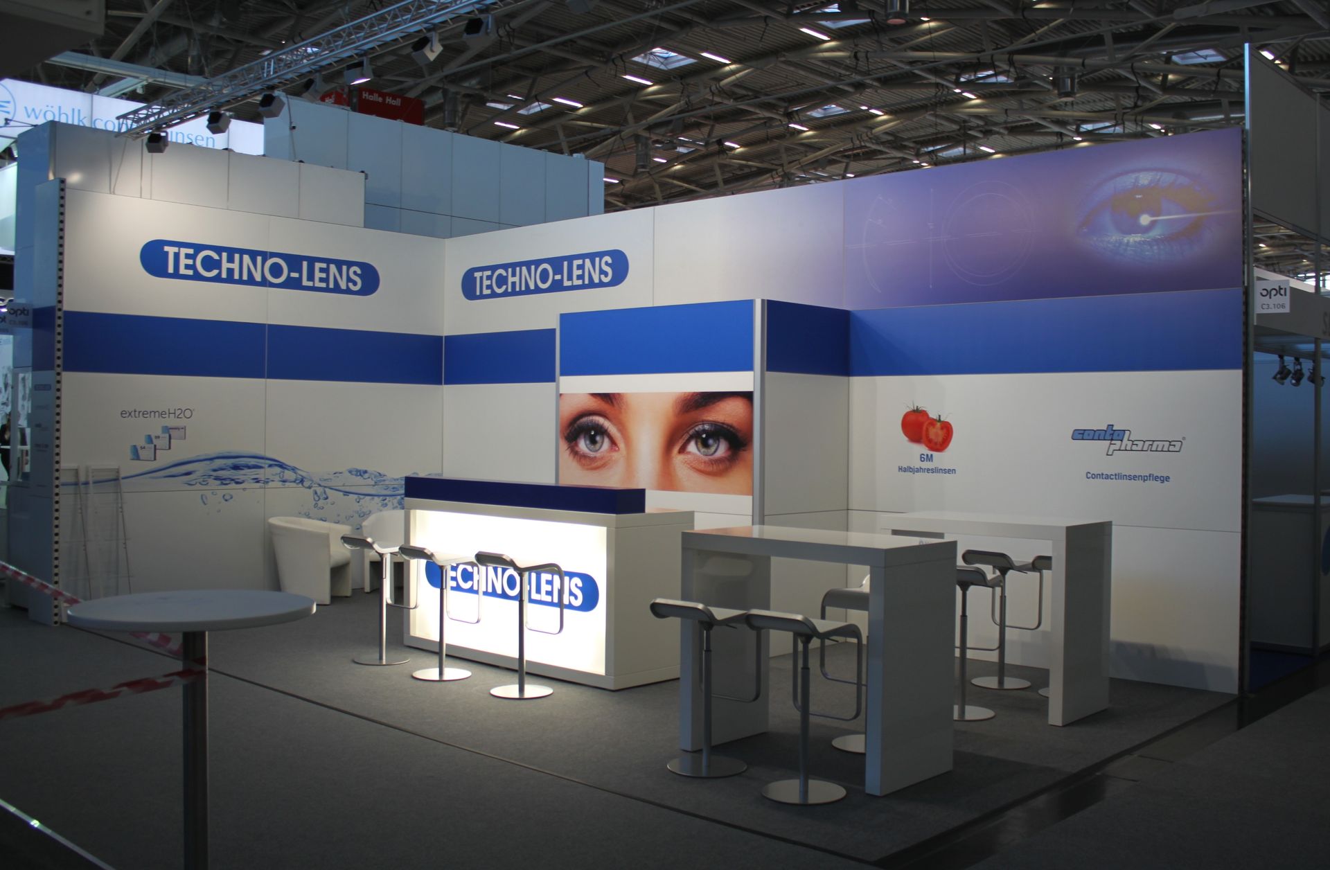 Techno-Lens-Messestand: blau-weißes Design, Produktbranding, Augengrafik, Barhocker und Tische.