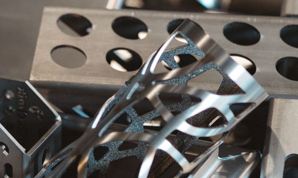 Lasergeschnittene Metallröhren mit komplizierten Mustern, die auf einem Metalltablett mit kreisförmigen Löchern ruhen.