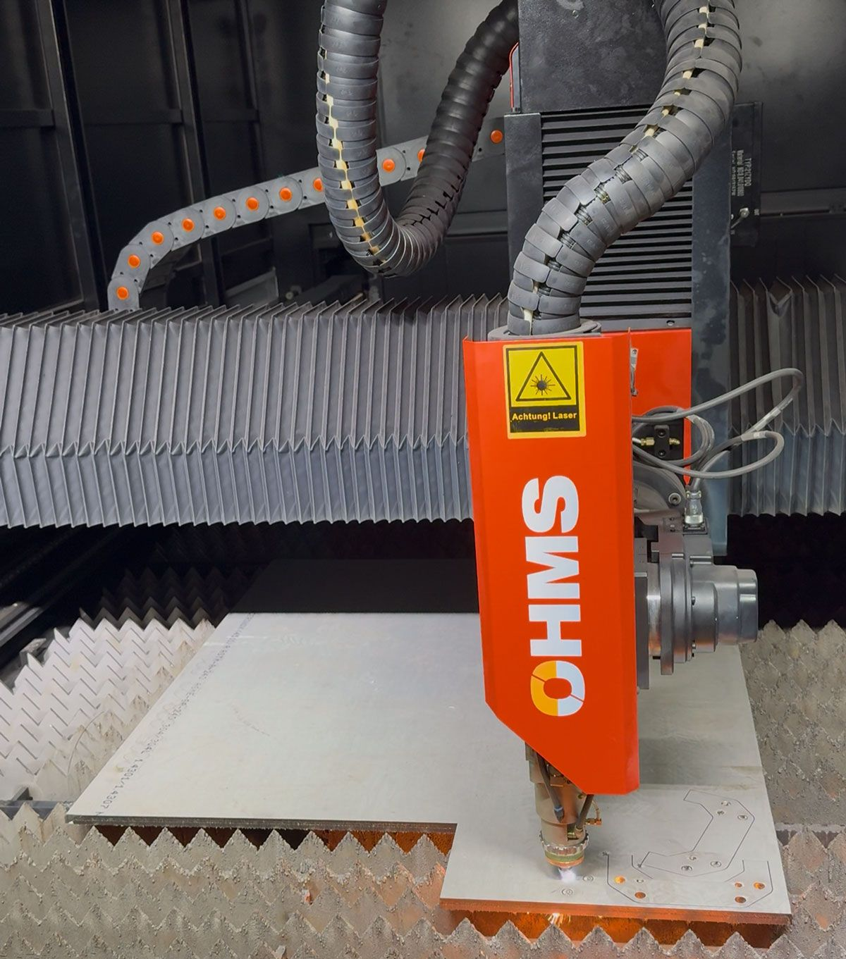Orangefarbenes, industriell lasergeschnittenes Metallblech. OHMS-Markenetikett sichtbar.