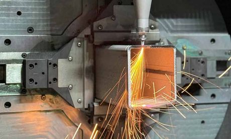 Eine Maschine schneidet ein Stück Metall, wobei Funken entstehen.