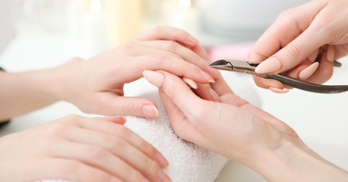 A una persona se le corta la mano con un cortaúñas mediante otra mano, que reposa sobre una toalla blanca.