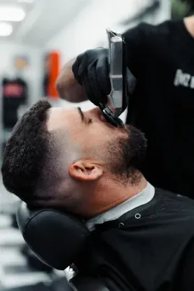 Un barbero le recorta la barba a un hombre con una maquinilla en una barbería. El hombre está sentado en una silla.