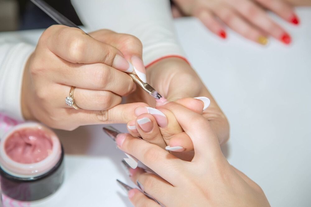 Una manicurista aplica esmalte de uñas en gel en las uñas de una clienta en un salón.